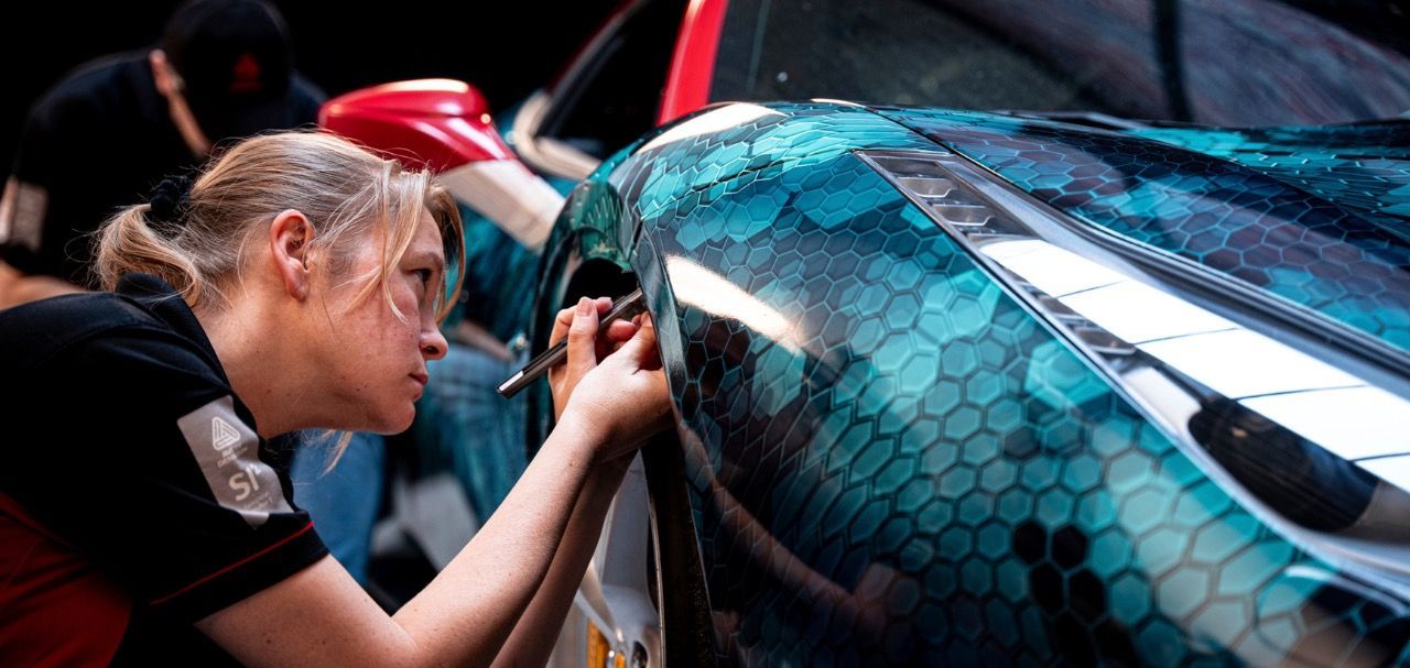 Woman wrapping a blue, hexagon-patterned print on car. Ferrari 488 GTB.