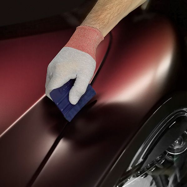 Hand applying Colorflow SWF film to Mclaran 600LT car with a blue squeegee, wearing a glove.
