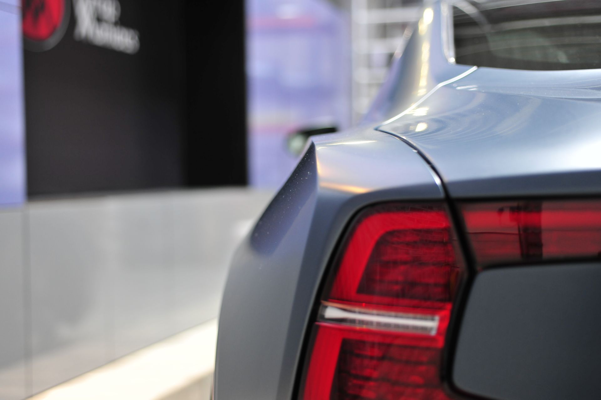Rear corner of a gray wrapped car. Polestar 1  with a red taillight, parked inside Wrap Maniacs workshop.