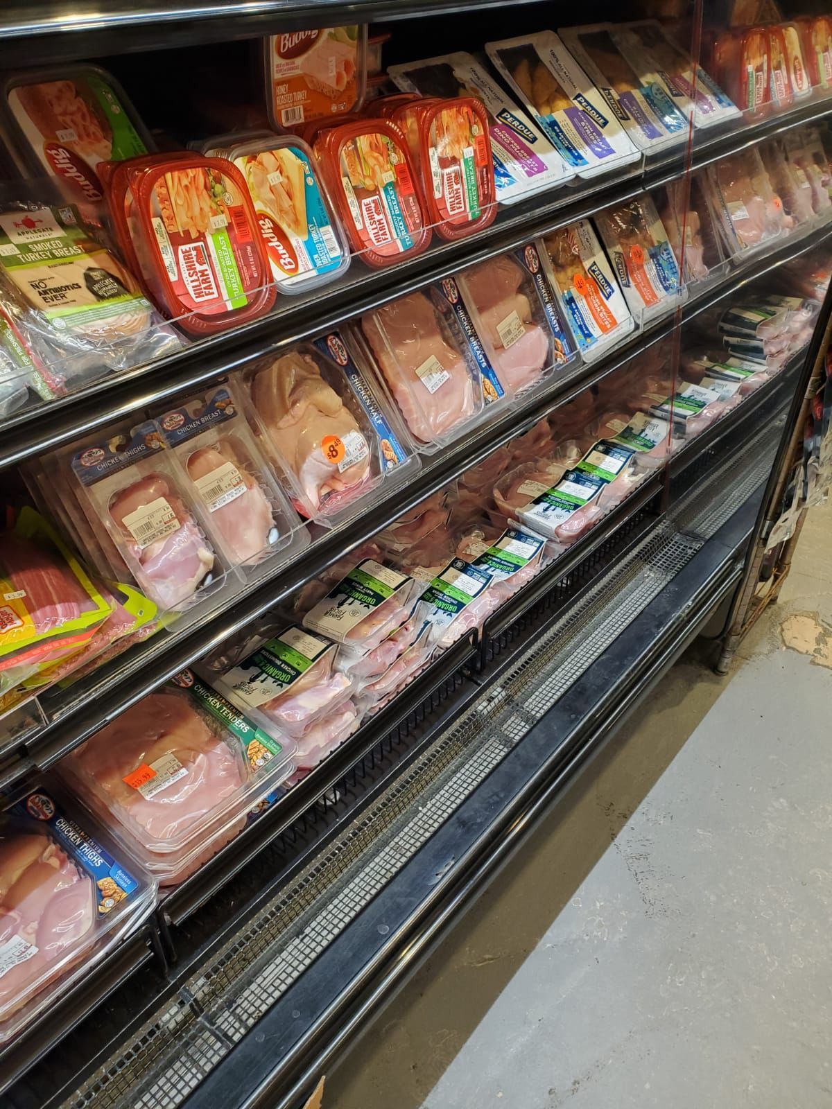 Grocery deli case with assorted packaged meats and prepared foods on refrigerated shelves.