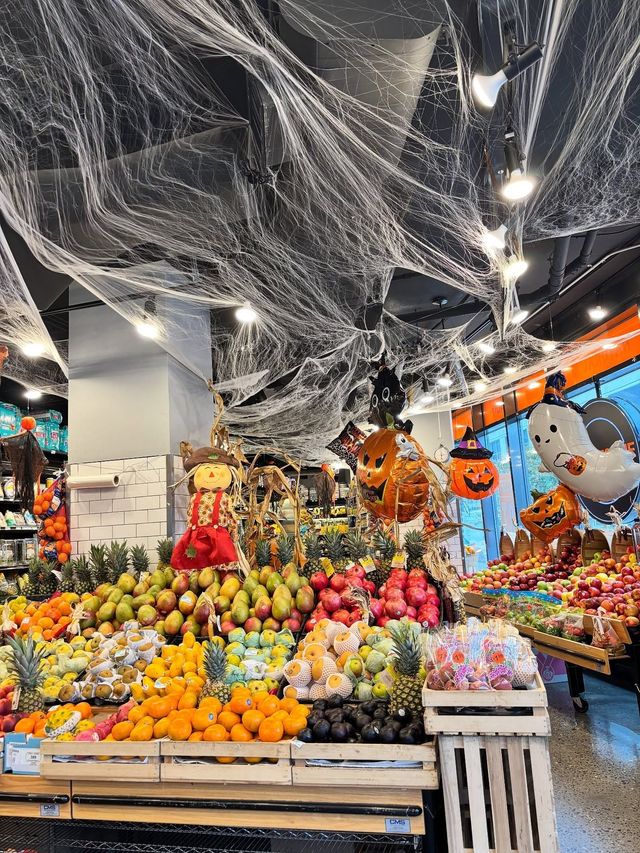 Halloween fruit display in a store, with pumpkins, apples, and hanging cobweb decorations