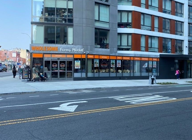 Corner storefront with orange signage on a city street, viewed from across the road.