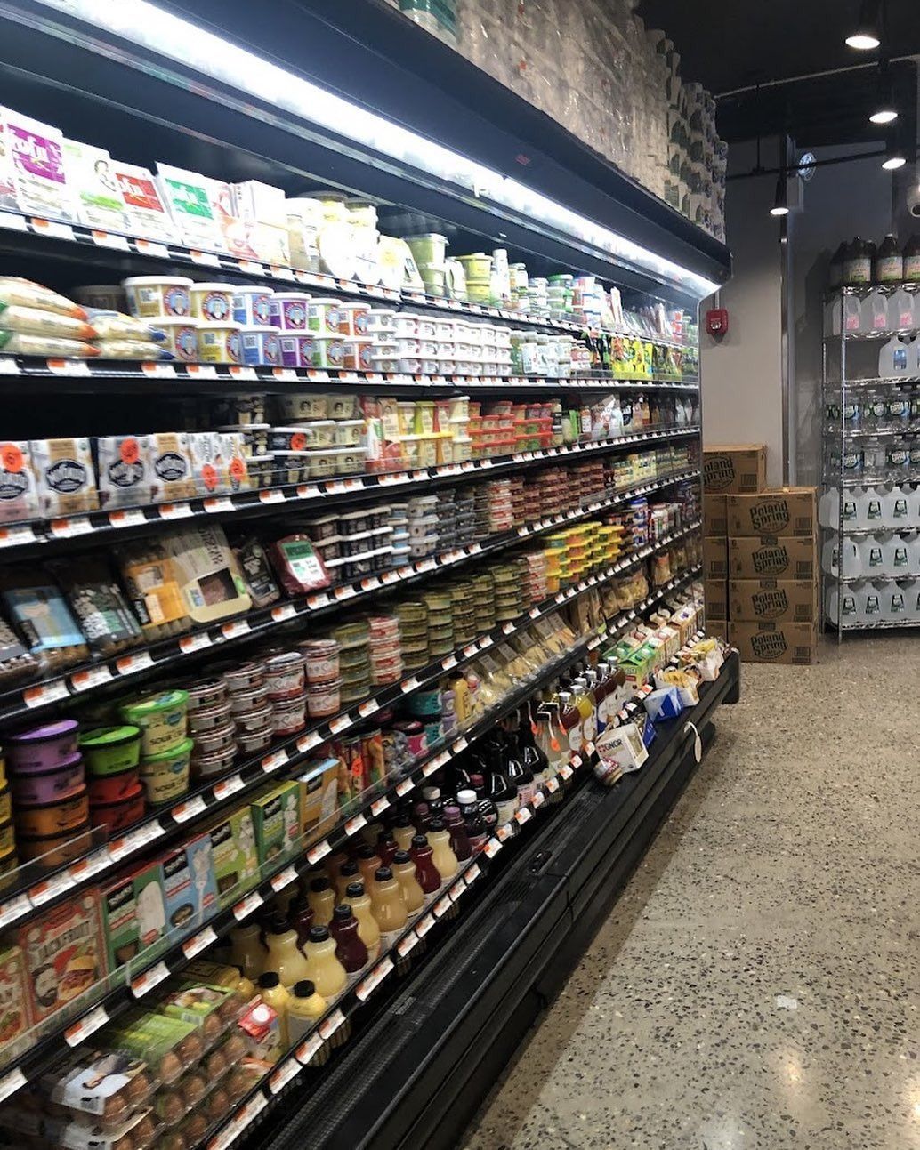 Grocery store aisle with refrigerated shelves stocked with packaged foods and drinks under bright lights