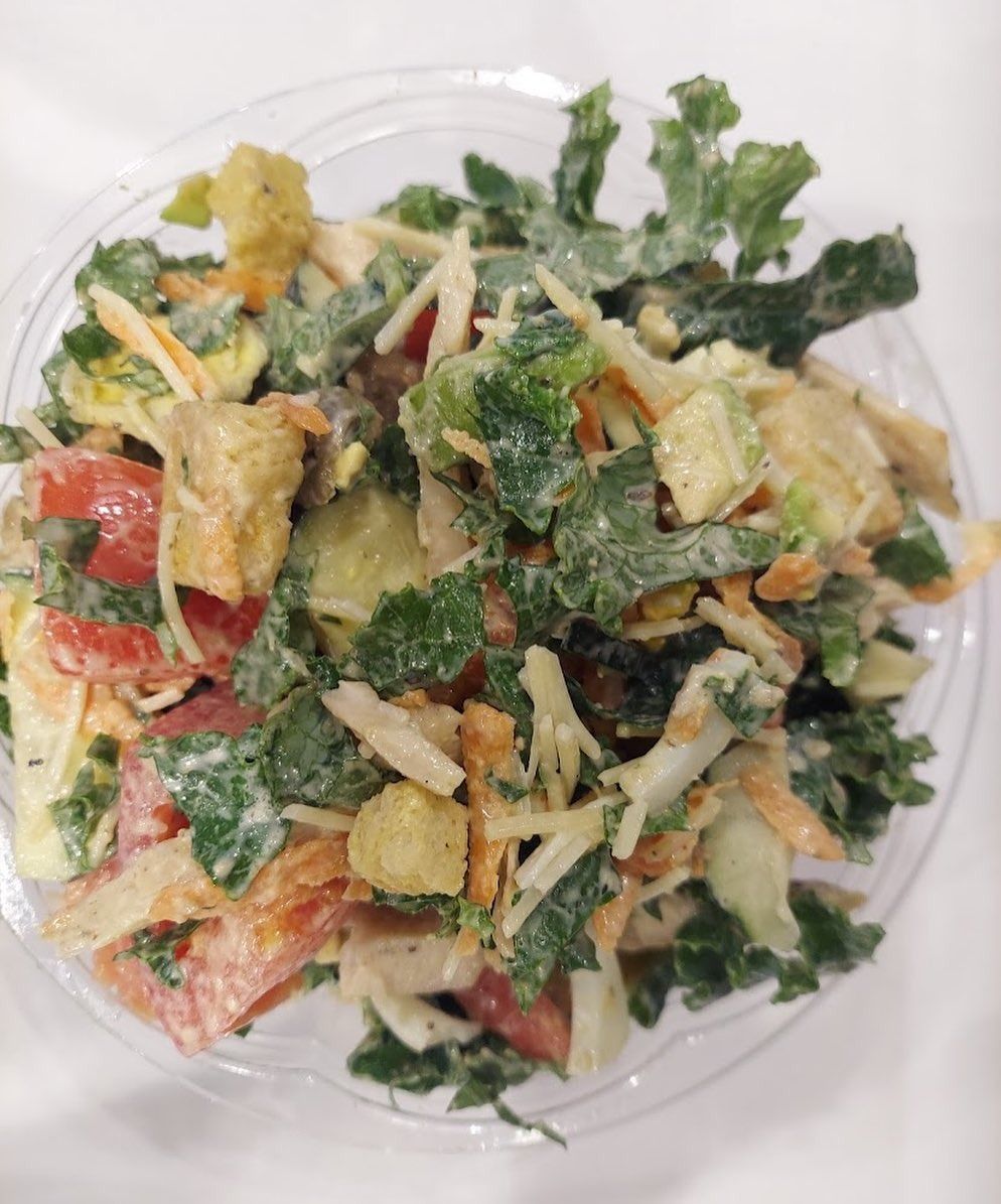 A plastic bowl of mixed salad with leafy greens, tomatoes, shredded carrots, and croutons.