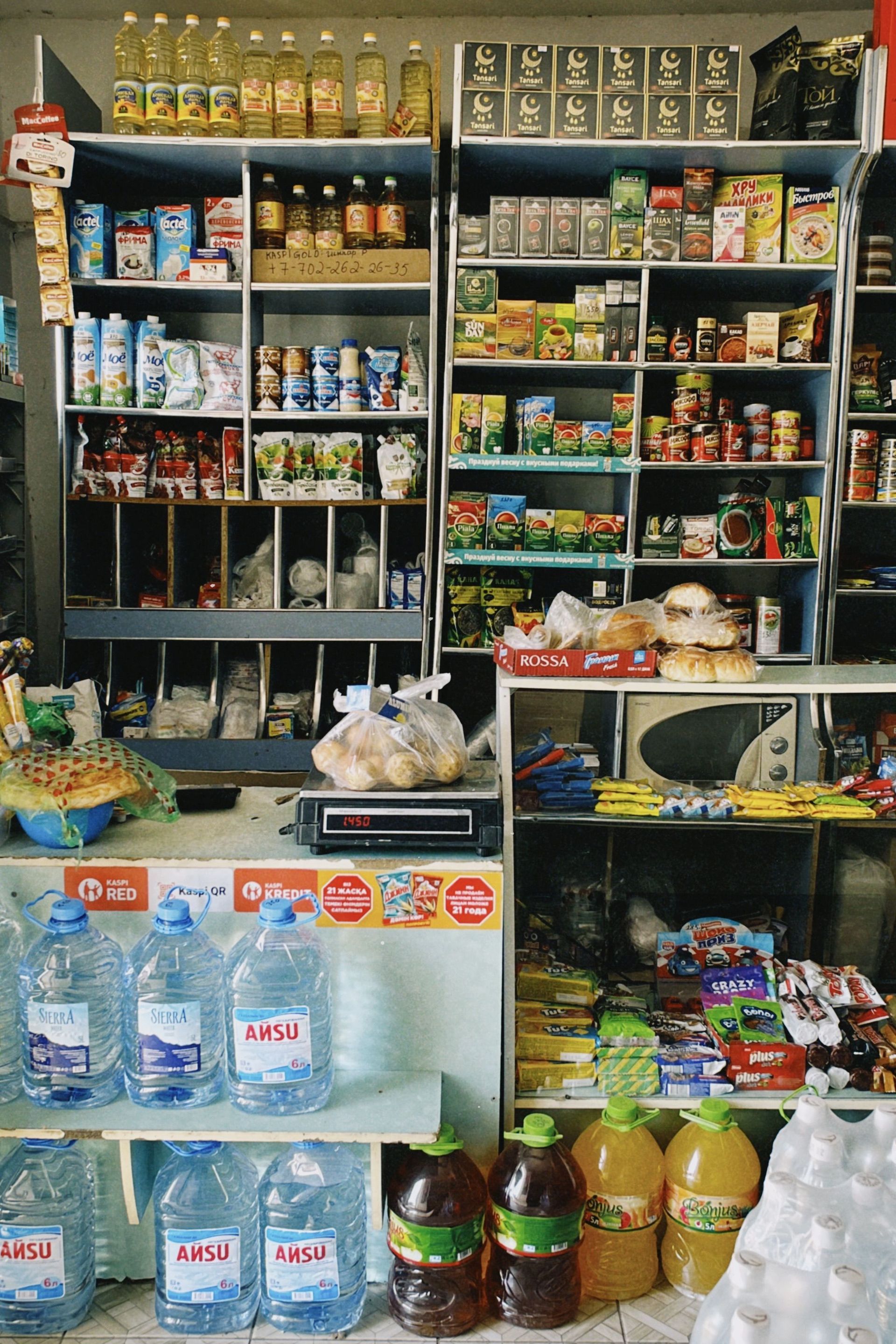 Small convenience store counter with shelves of snacks, drinks, and bottled water stacked inside.