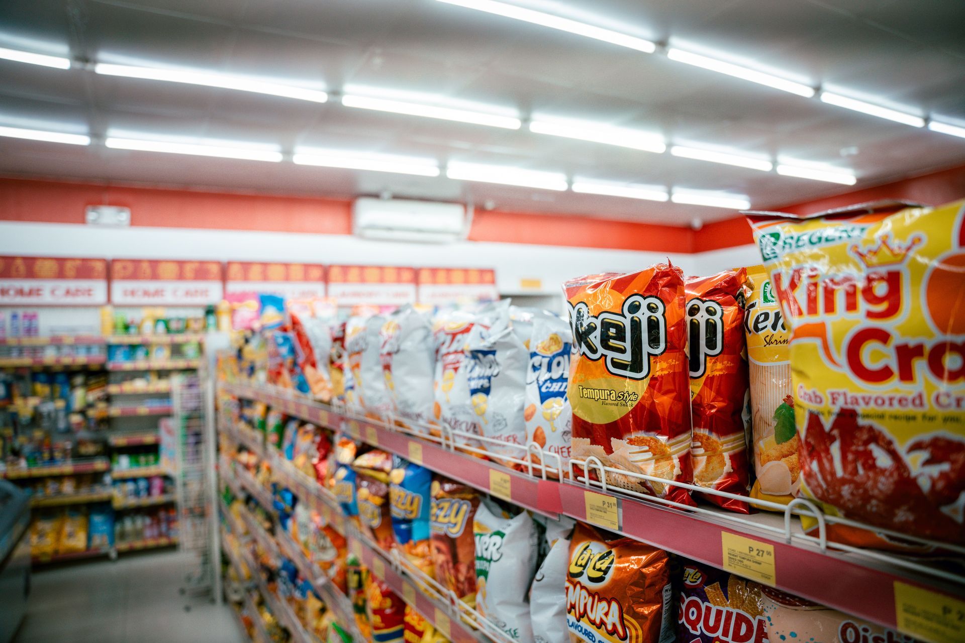 A grocery aisle with shelves of colorful snack bags and brightly lit ceiling lights