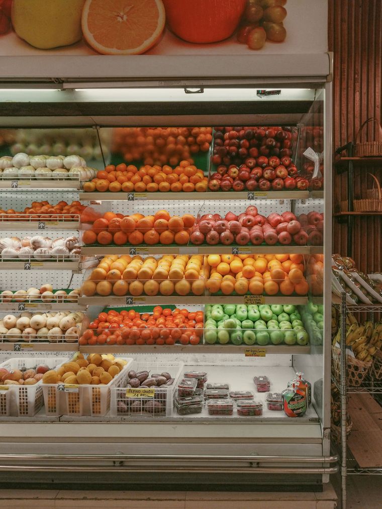 Refrigerated produce display with neatly arranged oranges, apples, grapes, and other fresh fruits