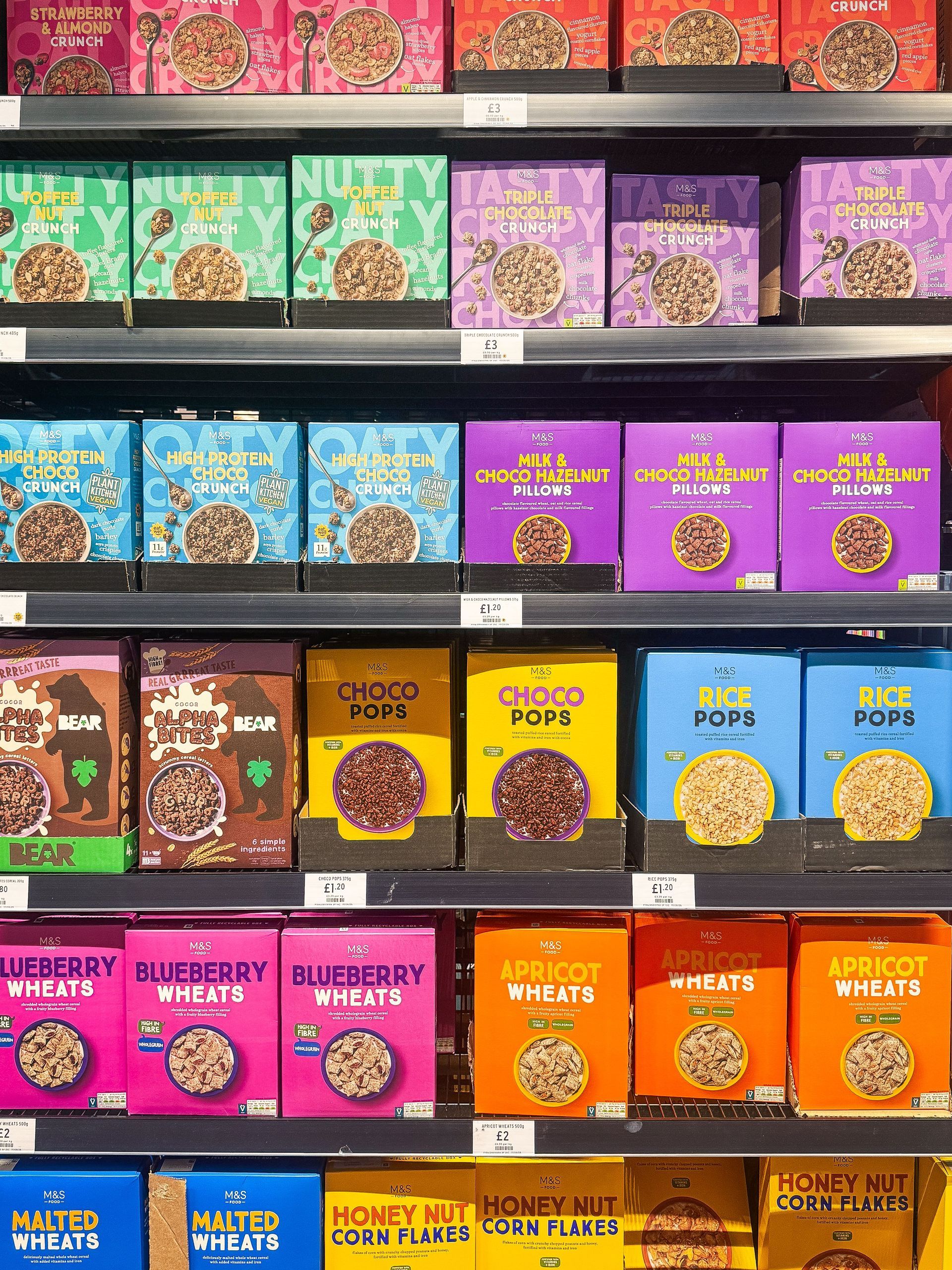 Colorful boxed popcorn bags stacked on grocery shelves in various flavors.