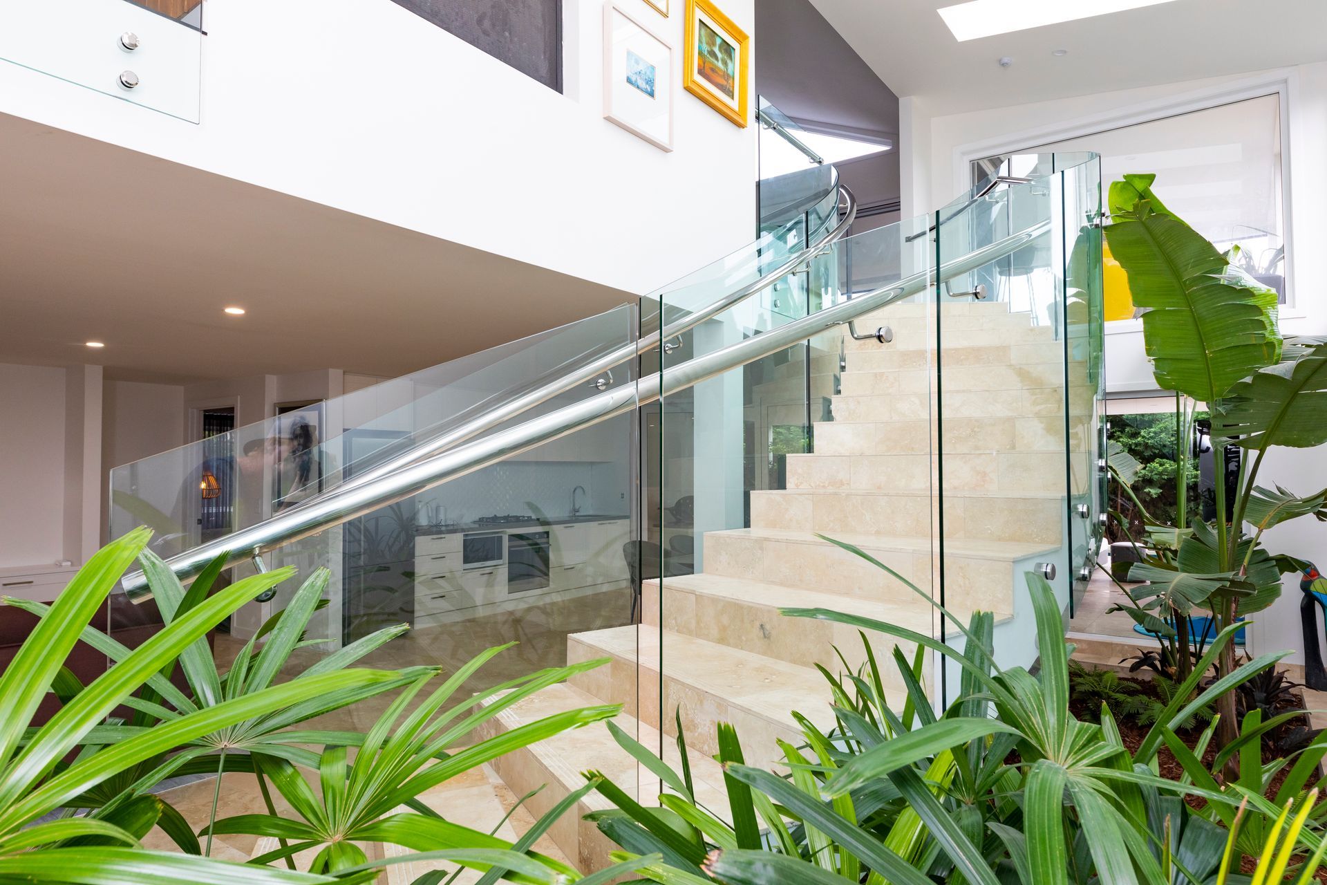 Curved Staircase Using Travertine Tiles With Glass And Metal Railings And Luscious Plants On Either Side — Star Glass Design Pty Ltd in Mayfield, NSW