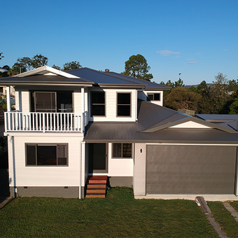 Two-story white house with a balcony, dark roof, and attached garage on a sunny day