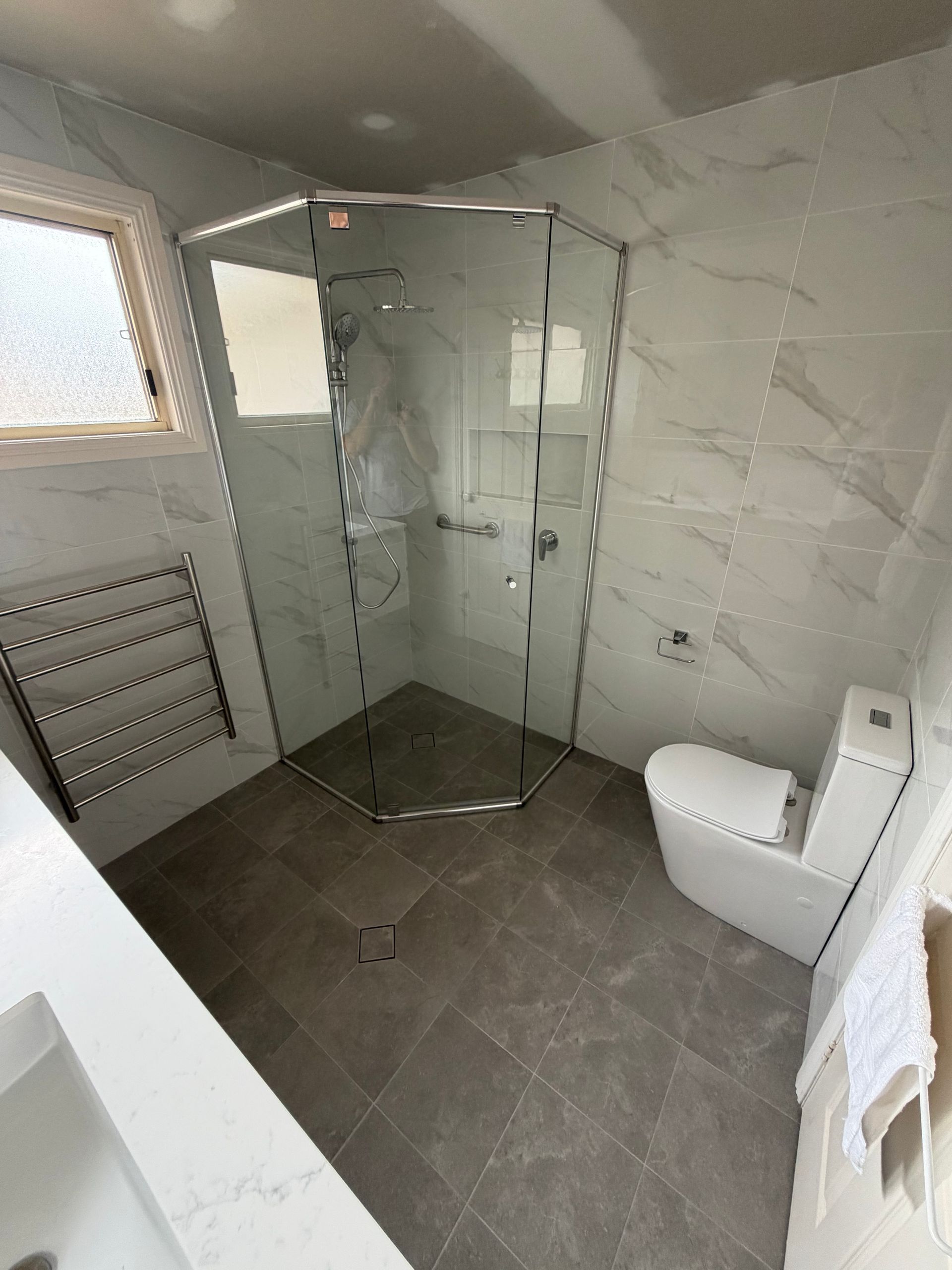 Modern bathroom with walk-in glass shower, gray tile walls and floor, and a white toilet