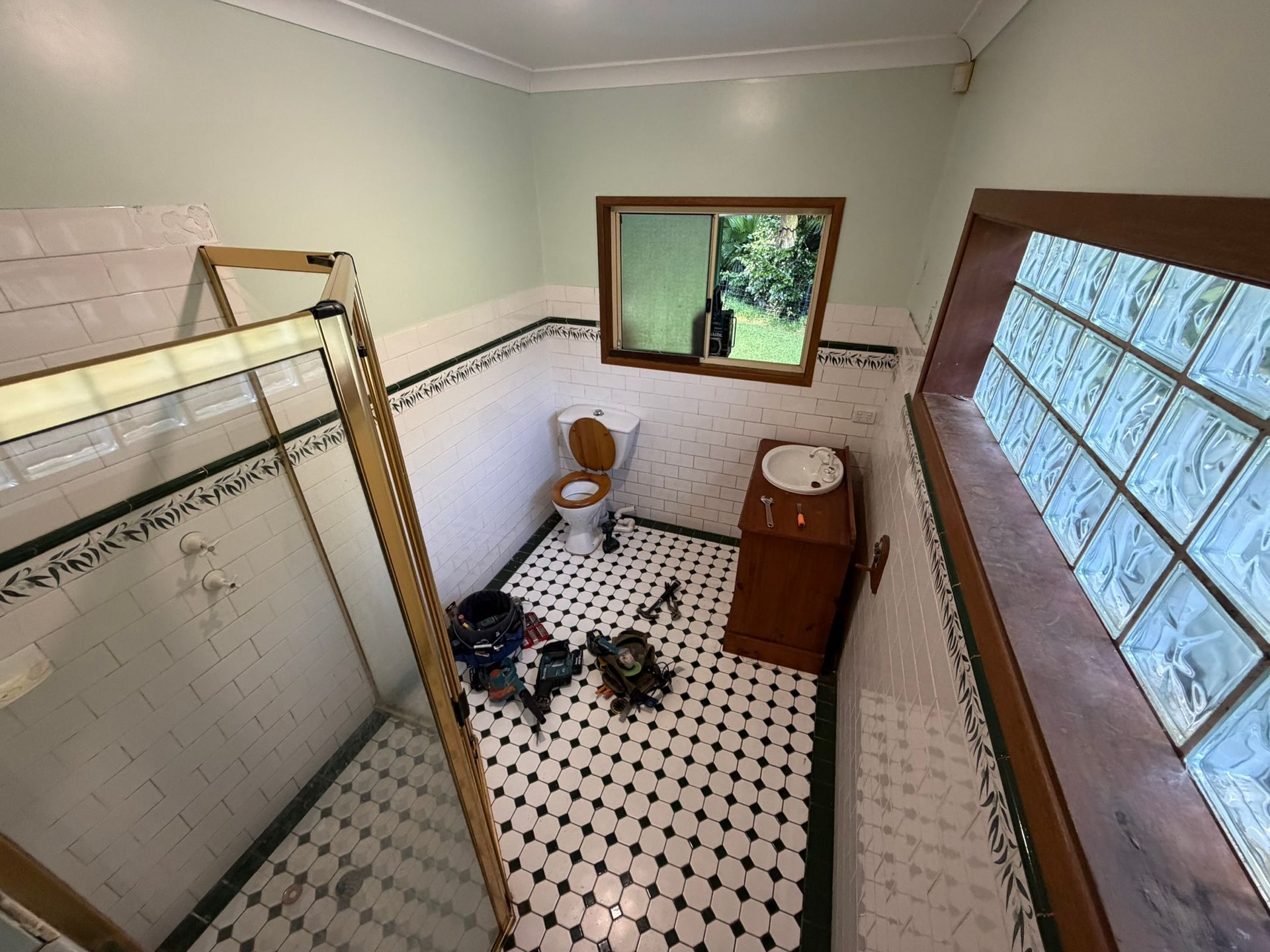 Small bathroom with tiled floor, shower stall, toilet, sink, and window letting in daylight.