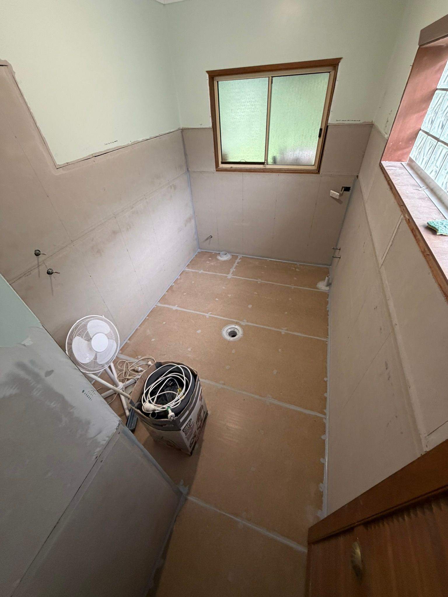 Small unfinished bathroom with tiled walls, window, and tools on the floor under renovation