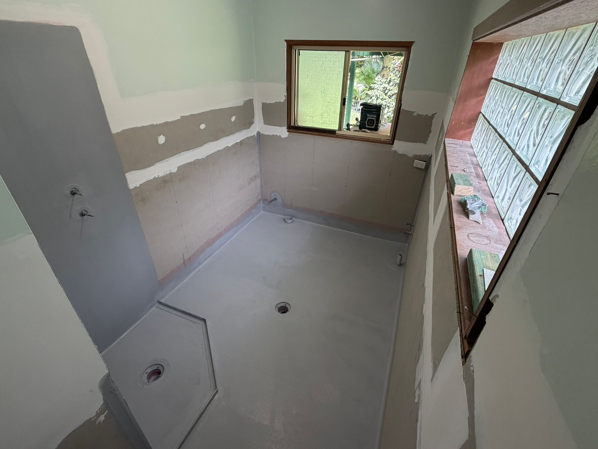 Small unfinished bathroom with white walls, toilet, sink, and window overlooking greenery.