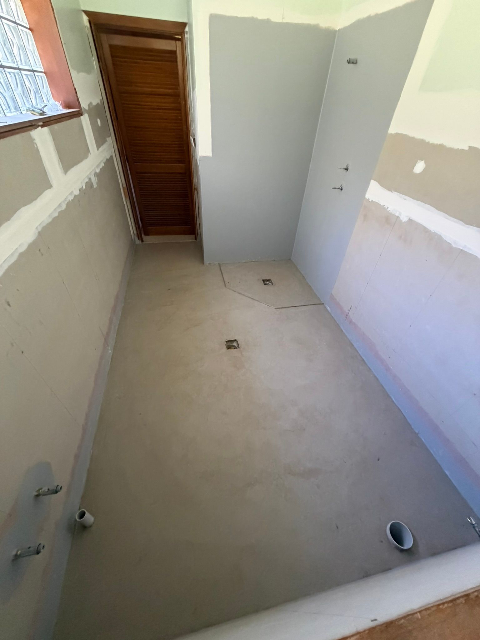 Empty narrow room under construction with unfinished walls, concrete floor, and a wooden door at the back