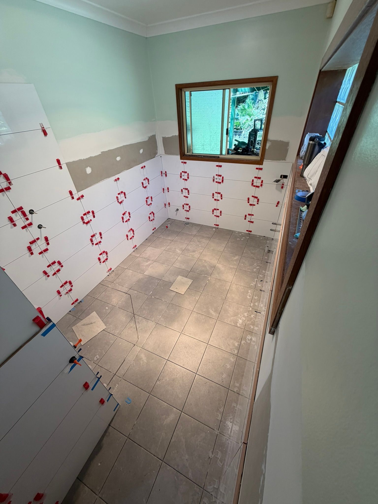 Empty kitchen with white tiled walls, mint green upper walls, and a small window above a tiled floor.