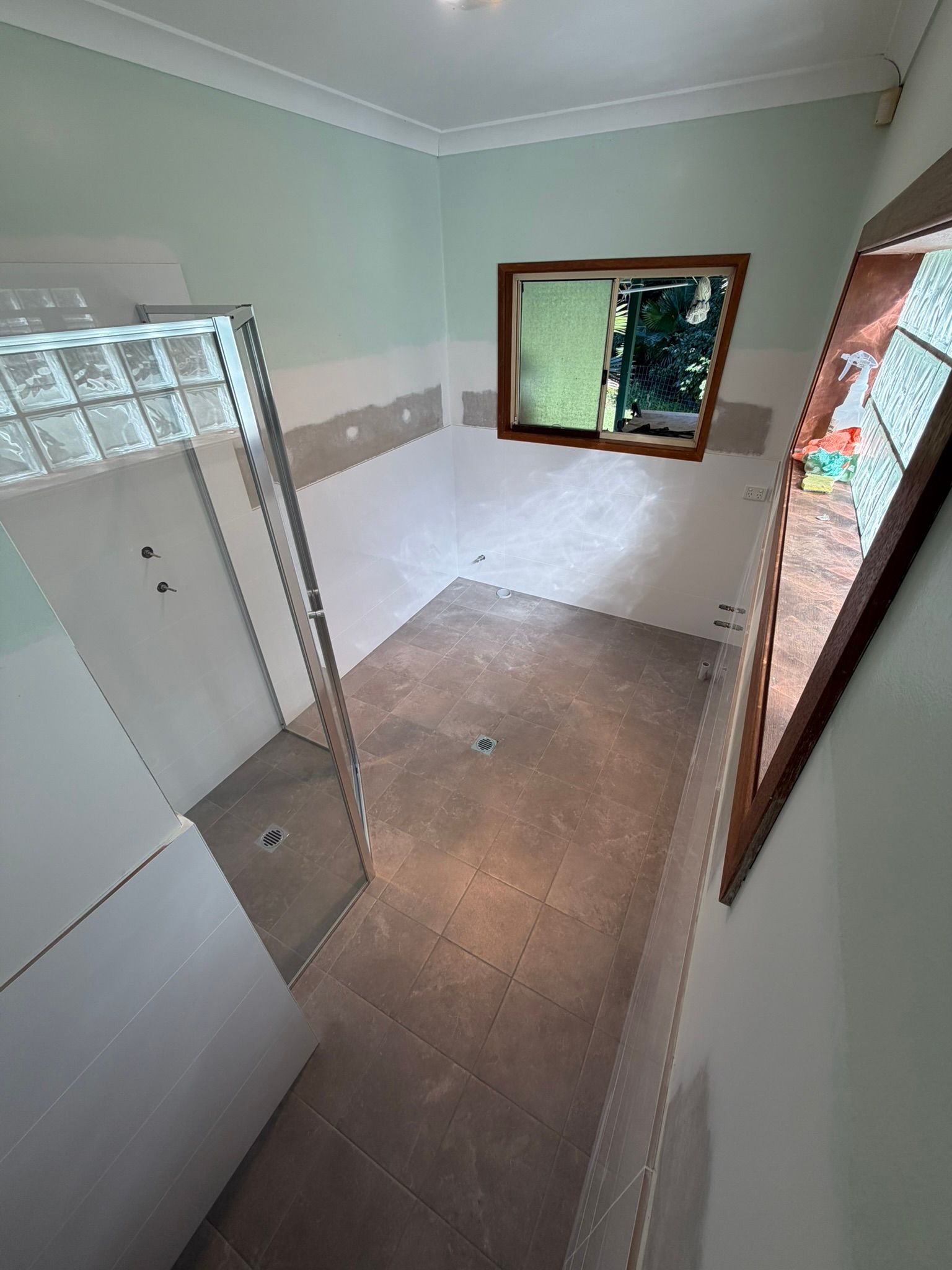 Small tiled bathroom with shower, toilet stall, window, and white walls with a gray accent strip.