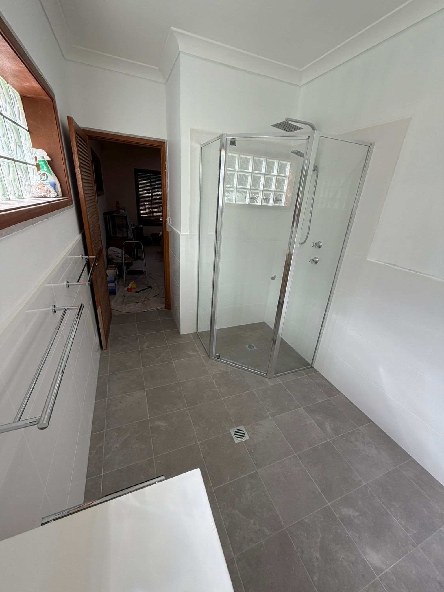 Small tiled bathroom with glass shower enclosure, white walls, and a window by the sink area