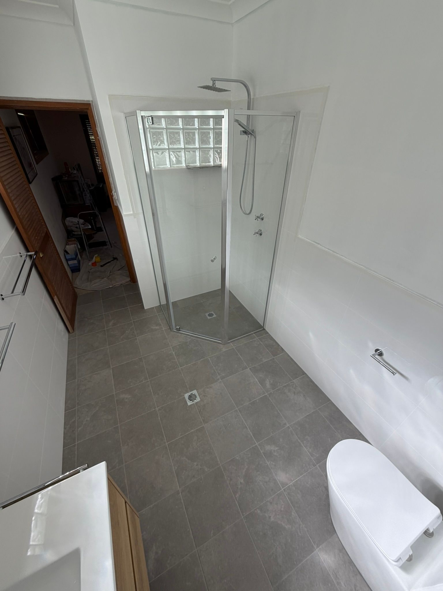 Small tiled bathroom with shower, toilet, sink, and a doorway to a dim hallway.
