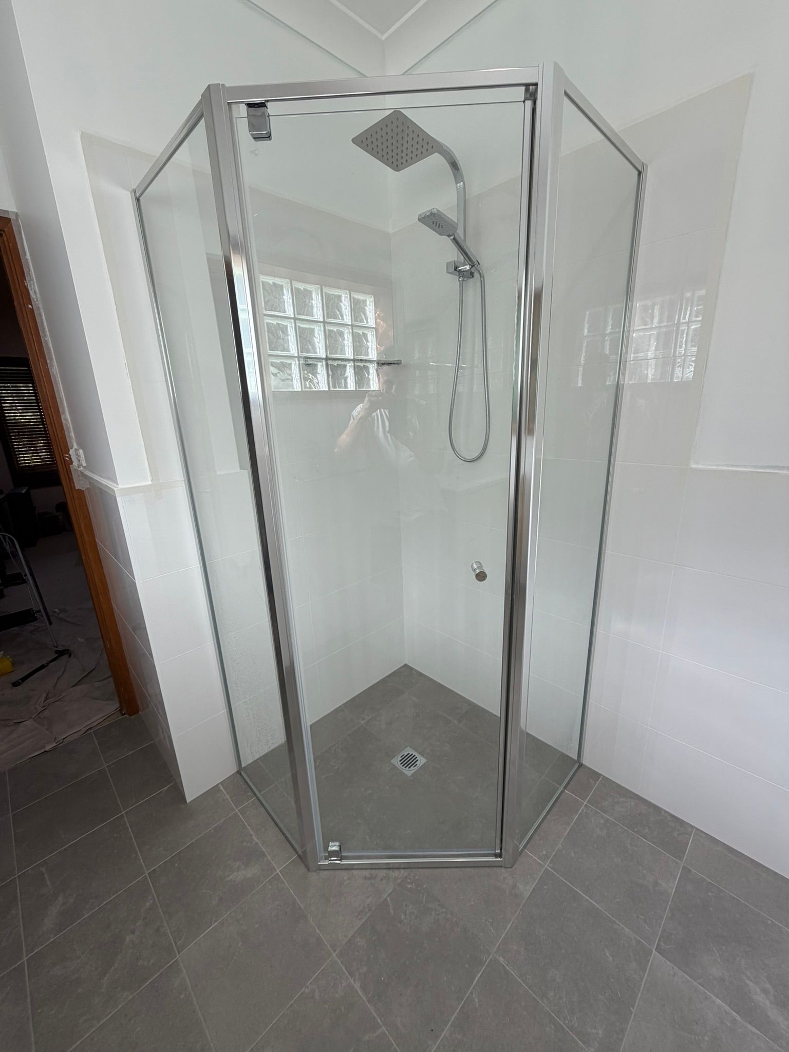 Corner walk-in shower with glass enclosure, gray tile floor, and wall-mounted showerhead.