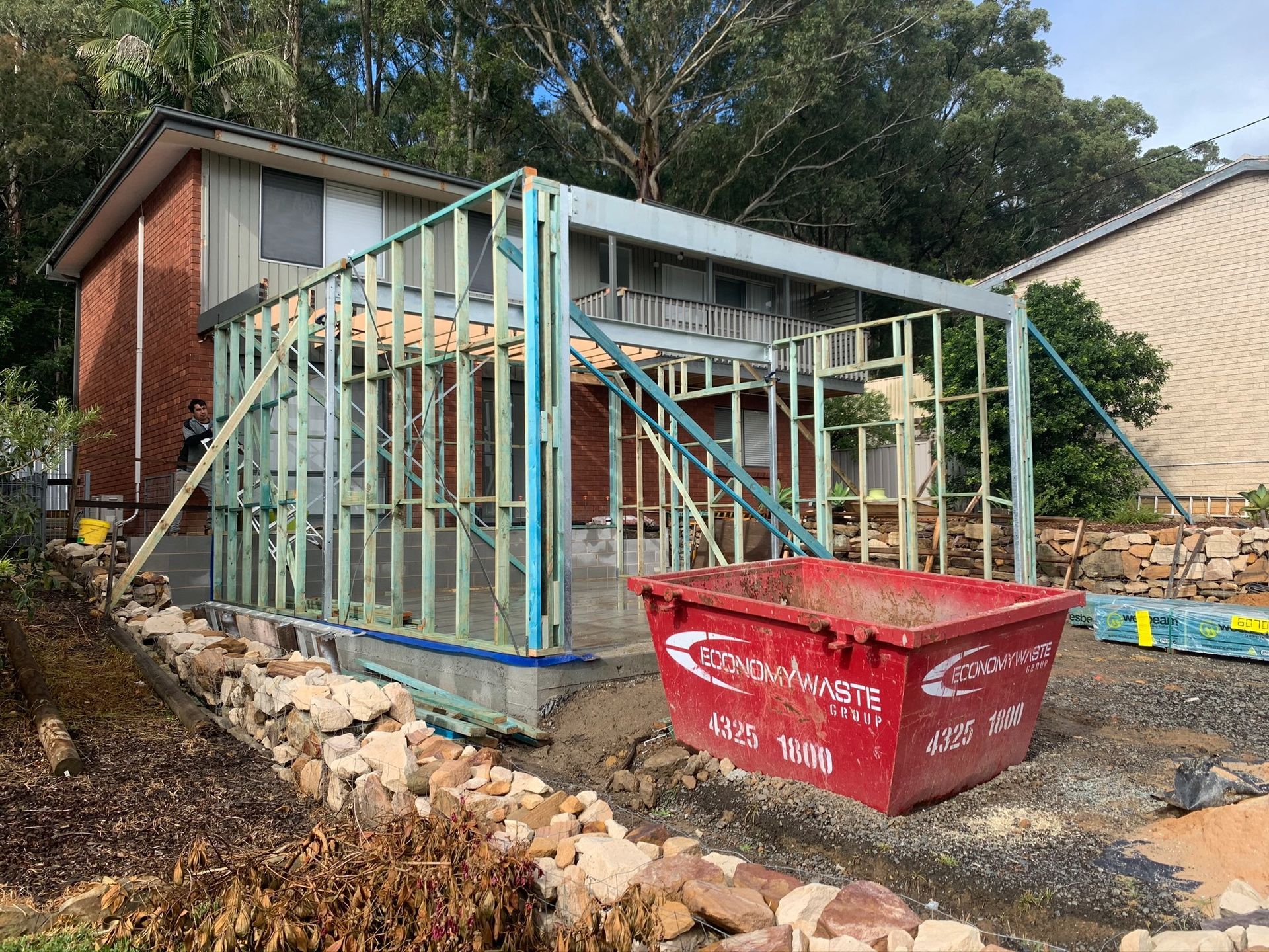 House under construction with exposed framing and a red dumpster in the foreground