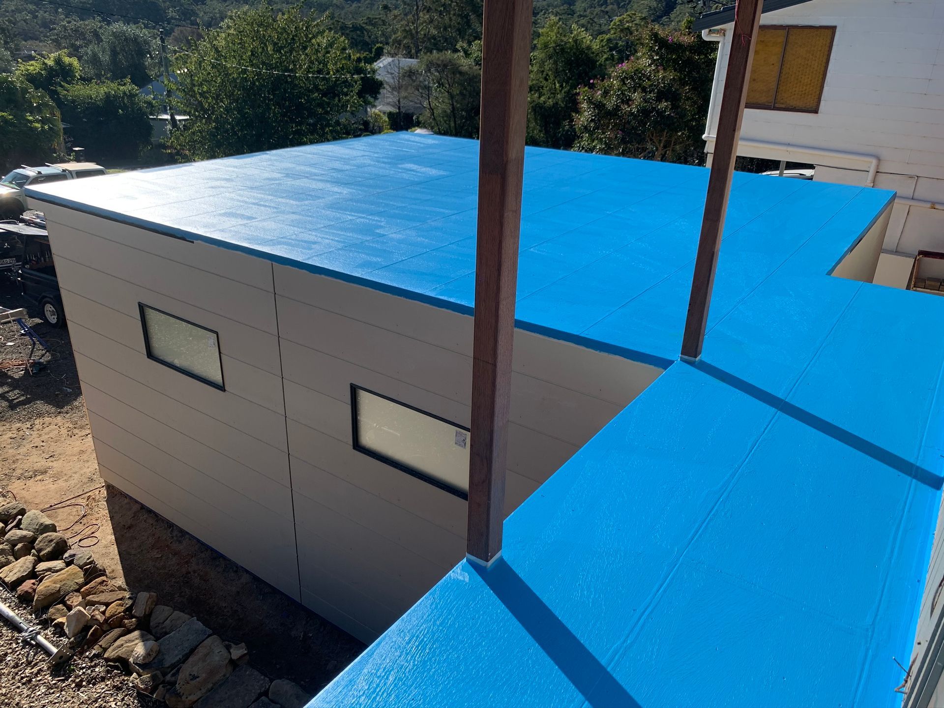 Small white building with bright blue roof panels beside rocks and a utility pole outdoors