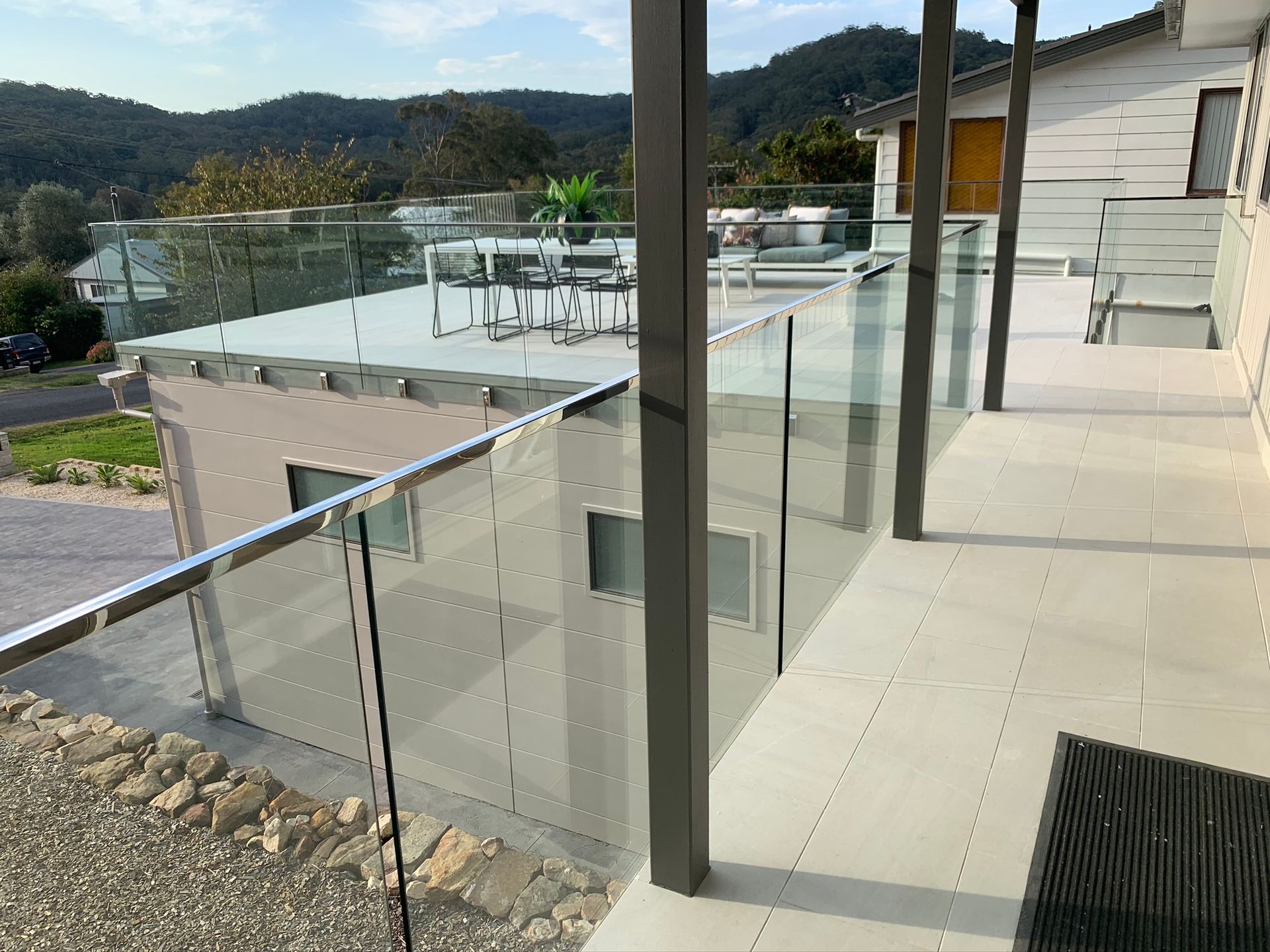 Modern house balcony with glass railing overlooking hills and a pool area