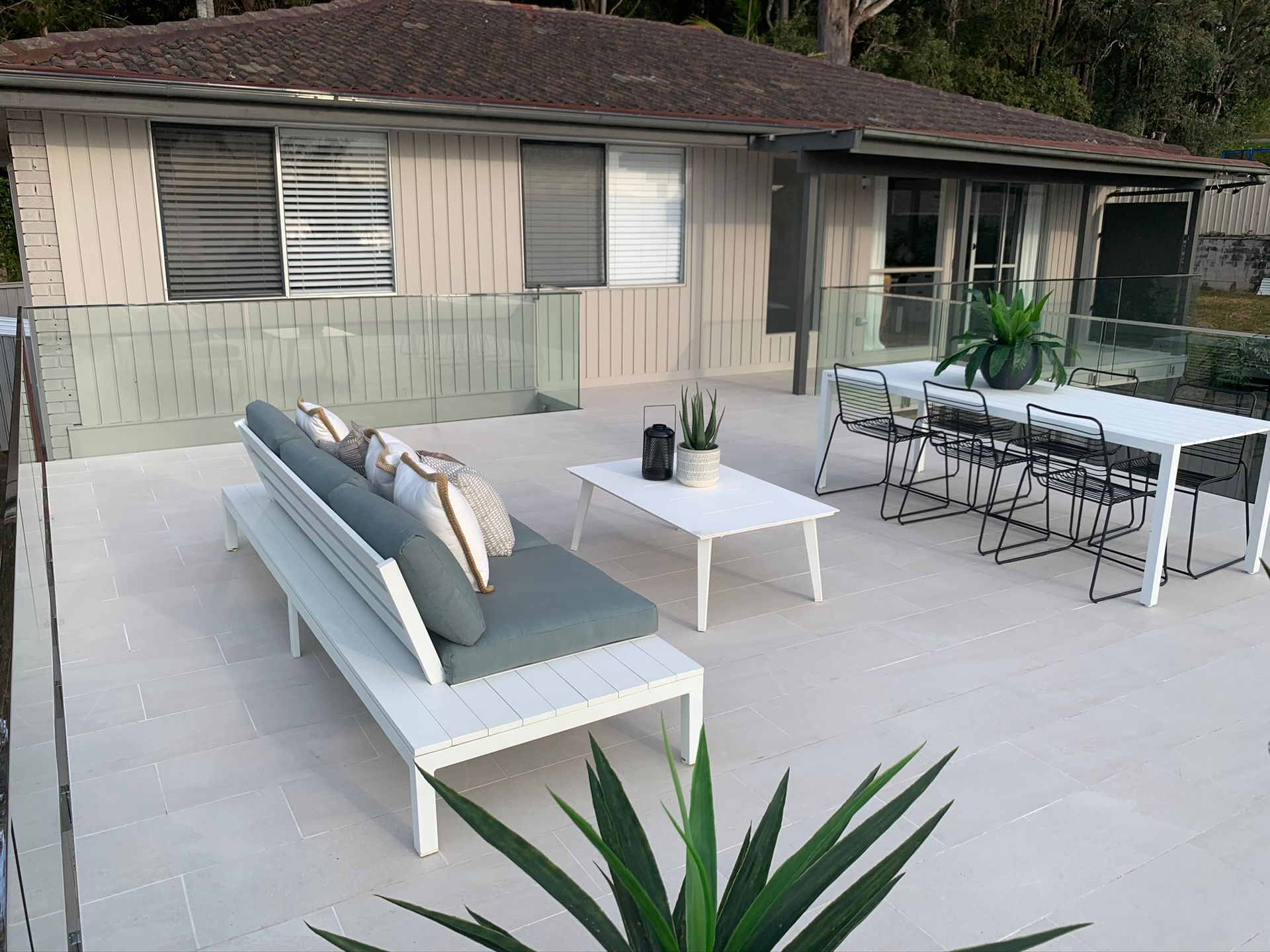 Patio with outdoor sofa, coffee table, dining set, and potted plants beside a house