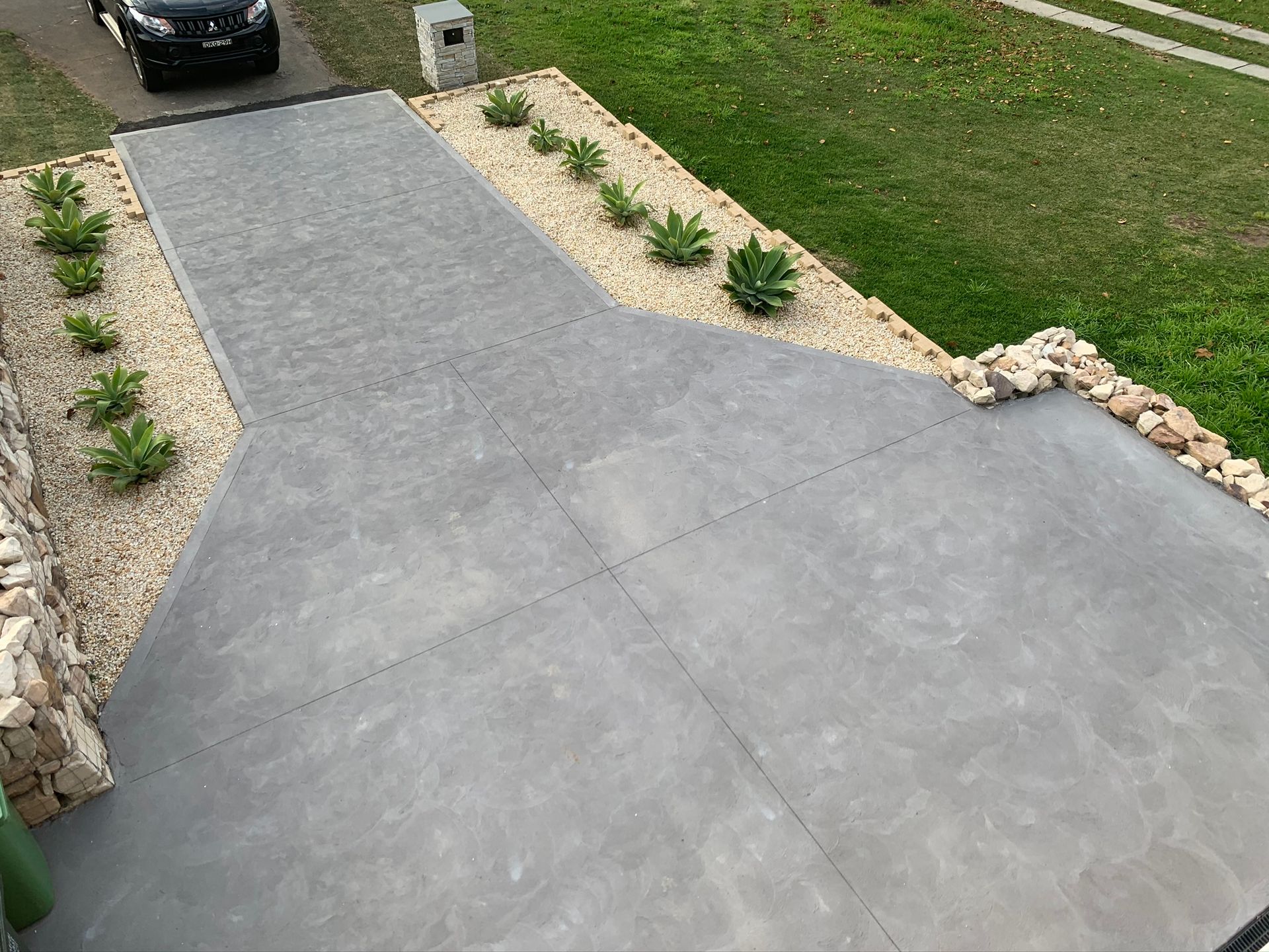 Fresh gray concrete driveway with stone-edged landscaping and a car at the top