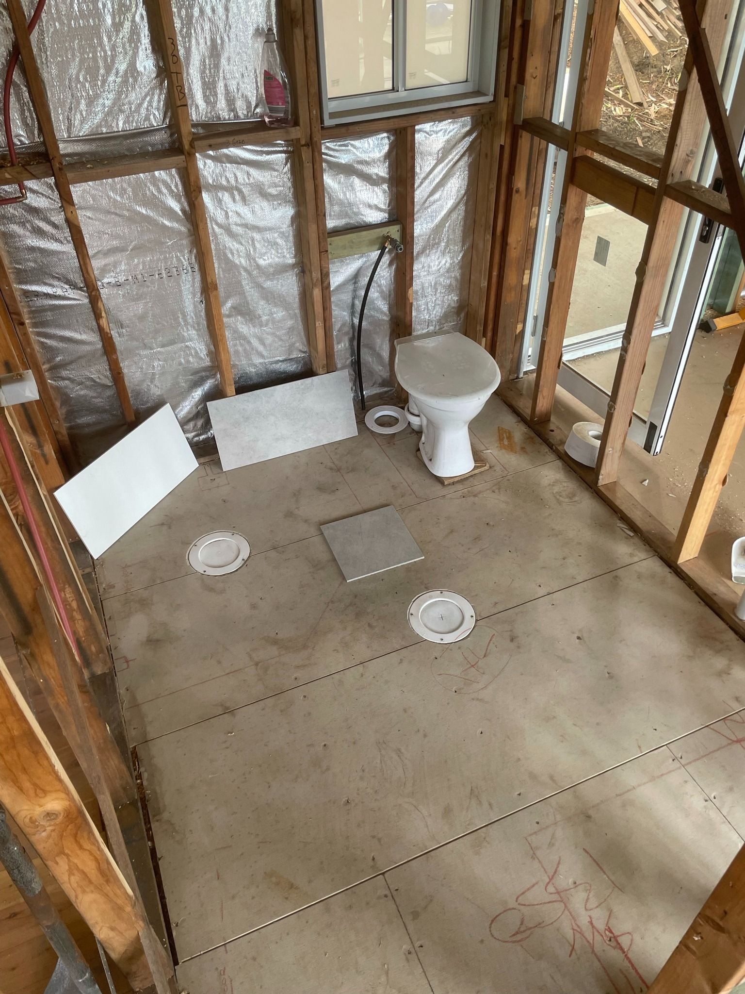 Unfinished bathroom with exposed framing, toilet, and shower floor drains under construction