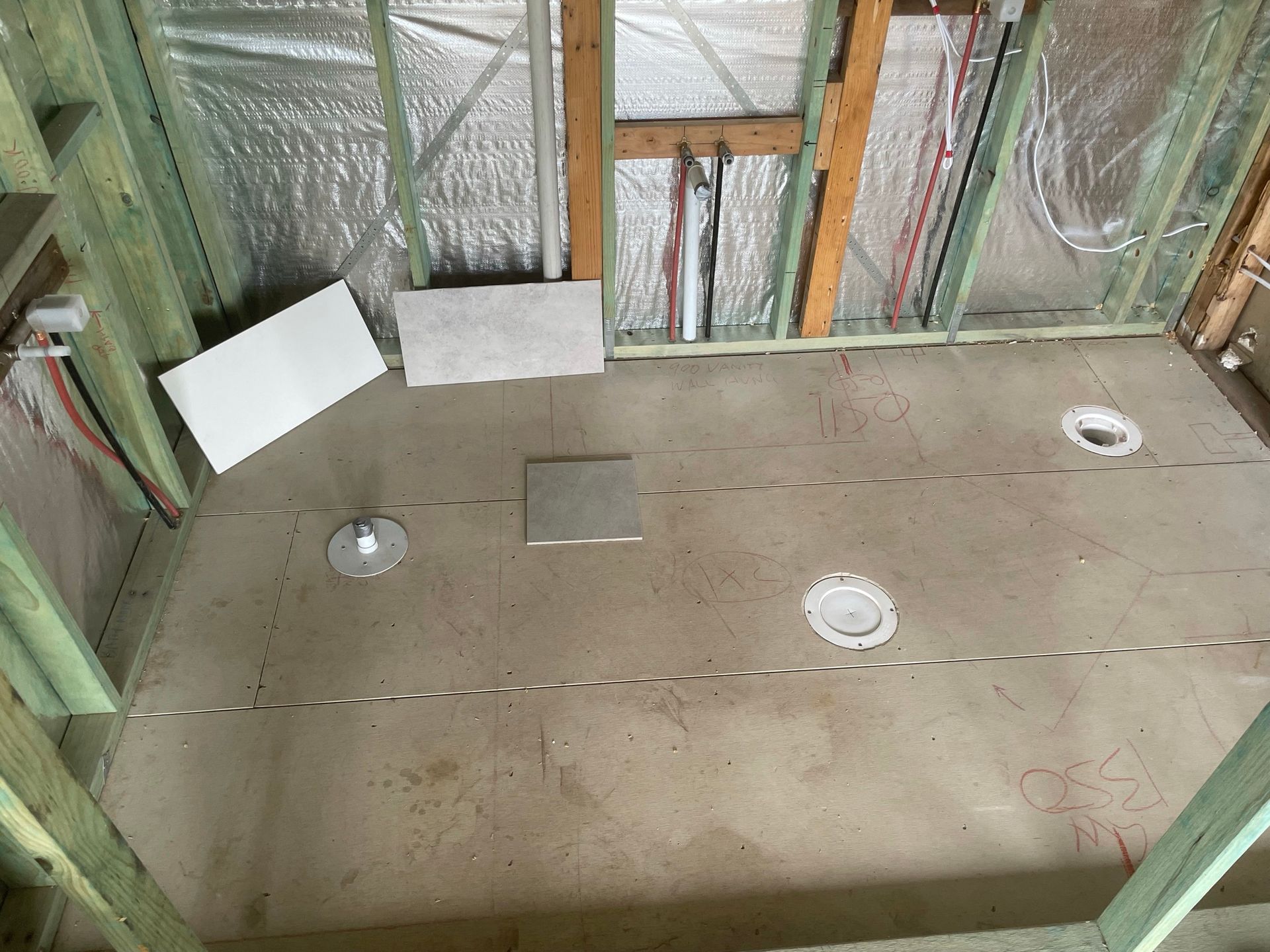 Unfinished room floor with taped seams, insulation in walls, and floor cutouts for plumbing fixtures
