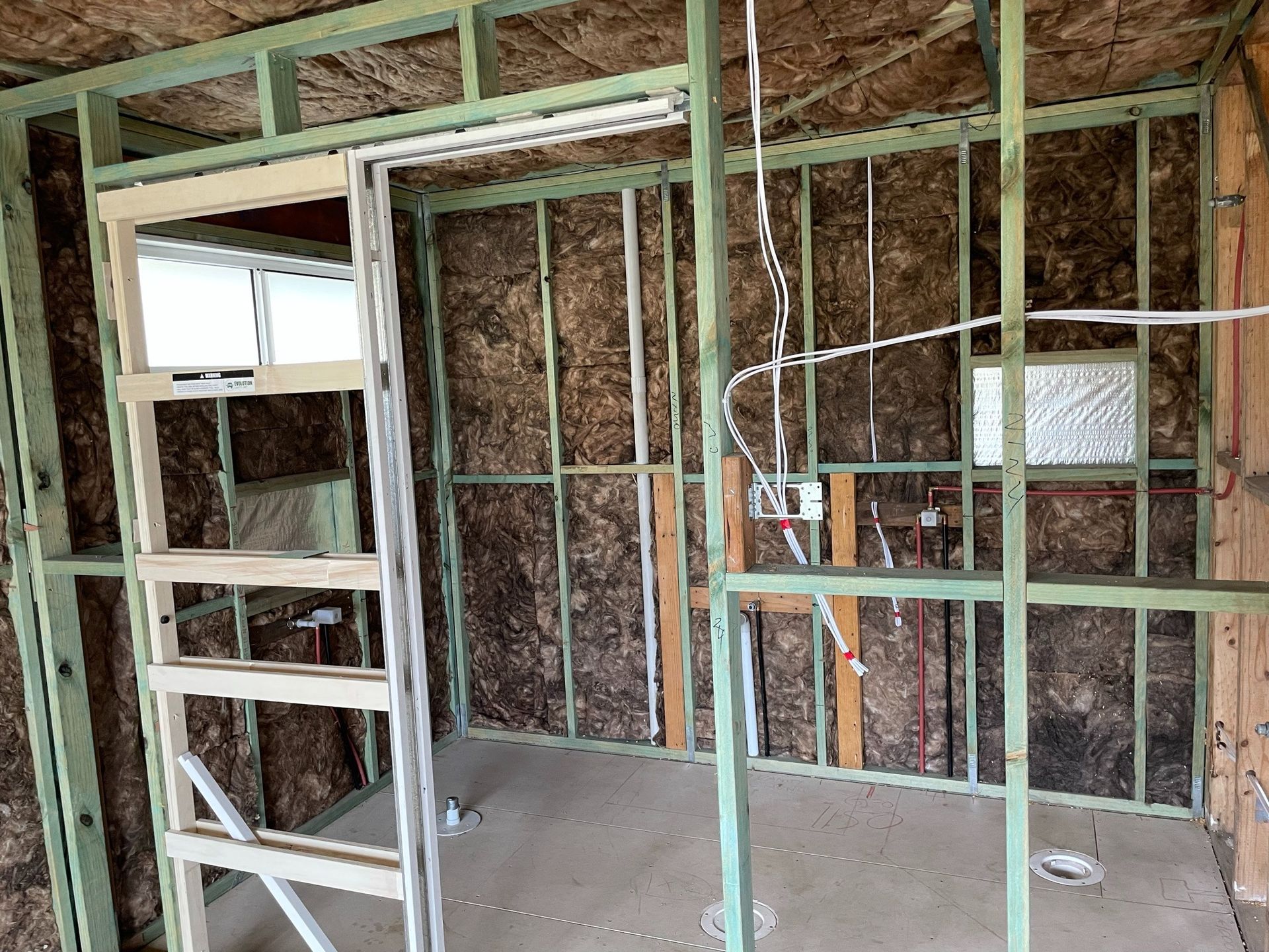Interior wall framing under construction with exposed studs and insulation in a bare room