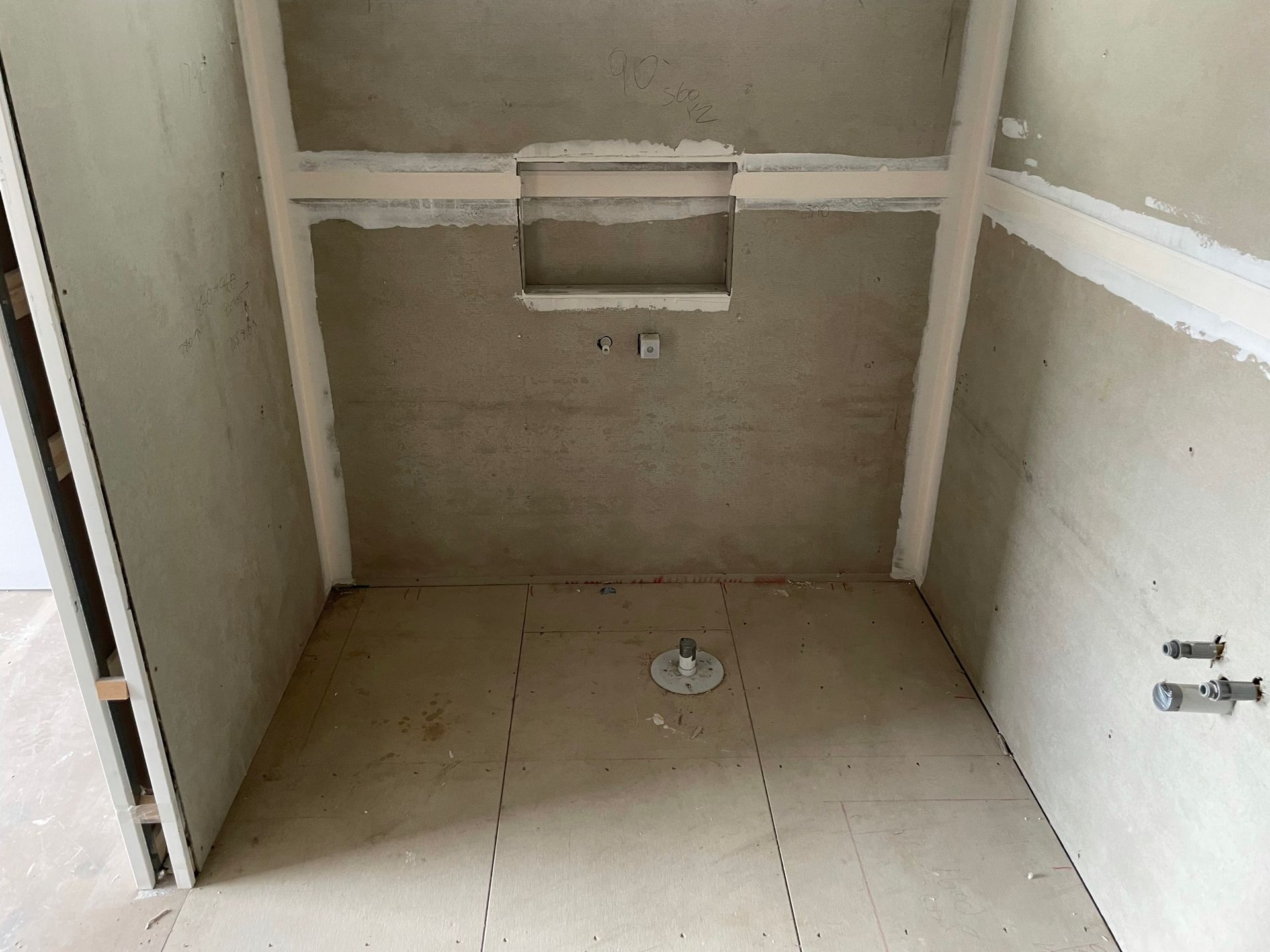 Small unfinished bathroom with tiled floor, wall-mounted toilet rough-in, and exposed plumbing fixtures.