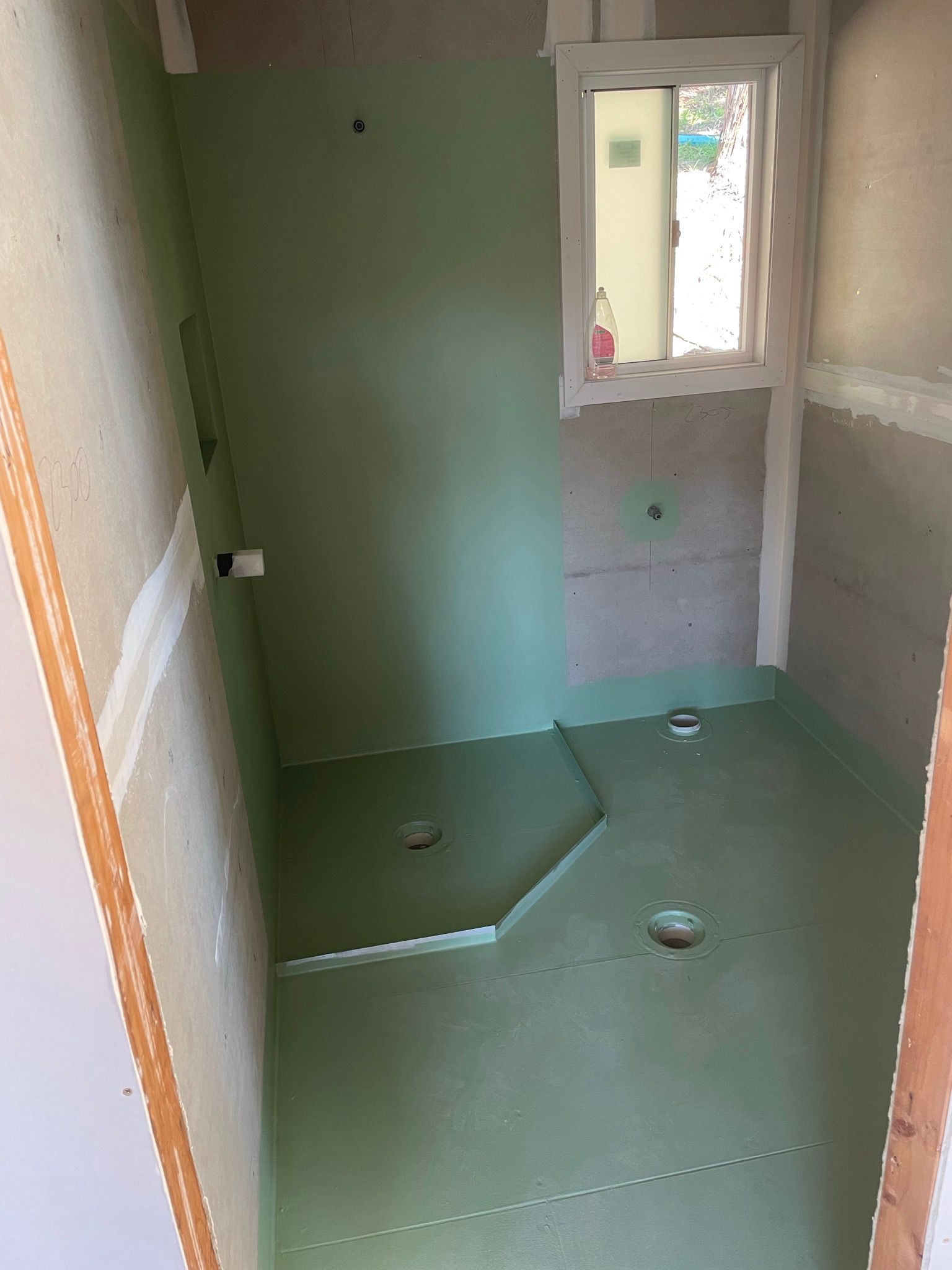 Empty shower room with green waterproof flooring, tiled walls, and a small window