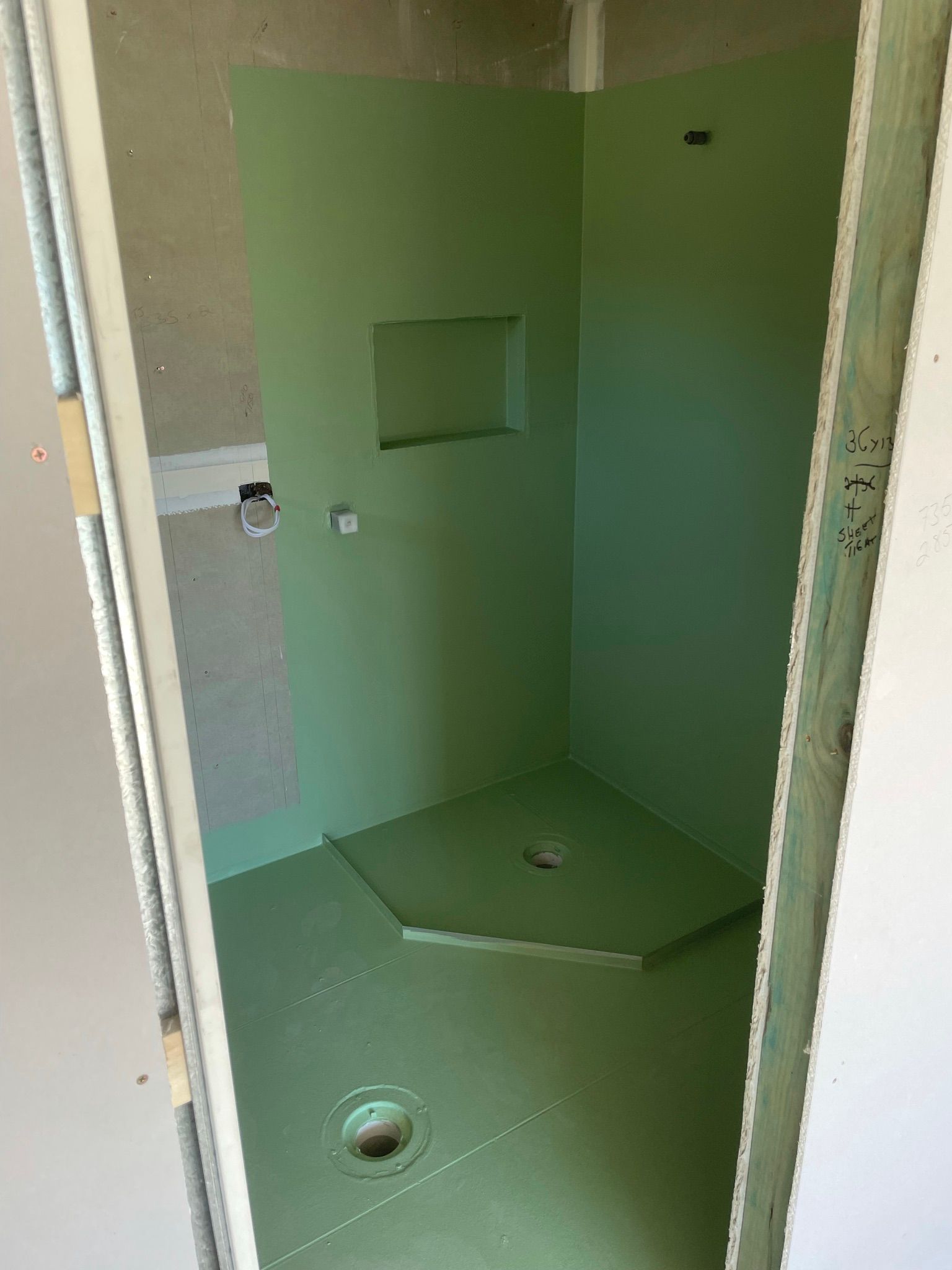 Empty green shower stall with a built-in shelf and drain hole in a small bathroom area