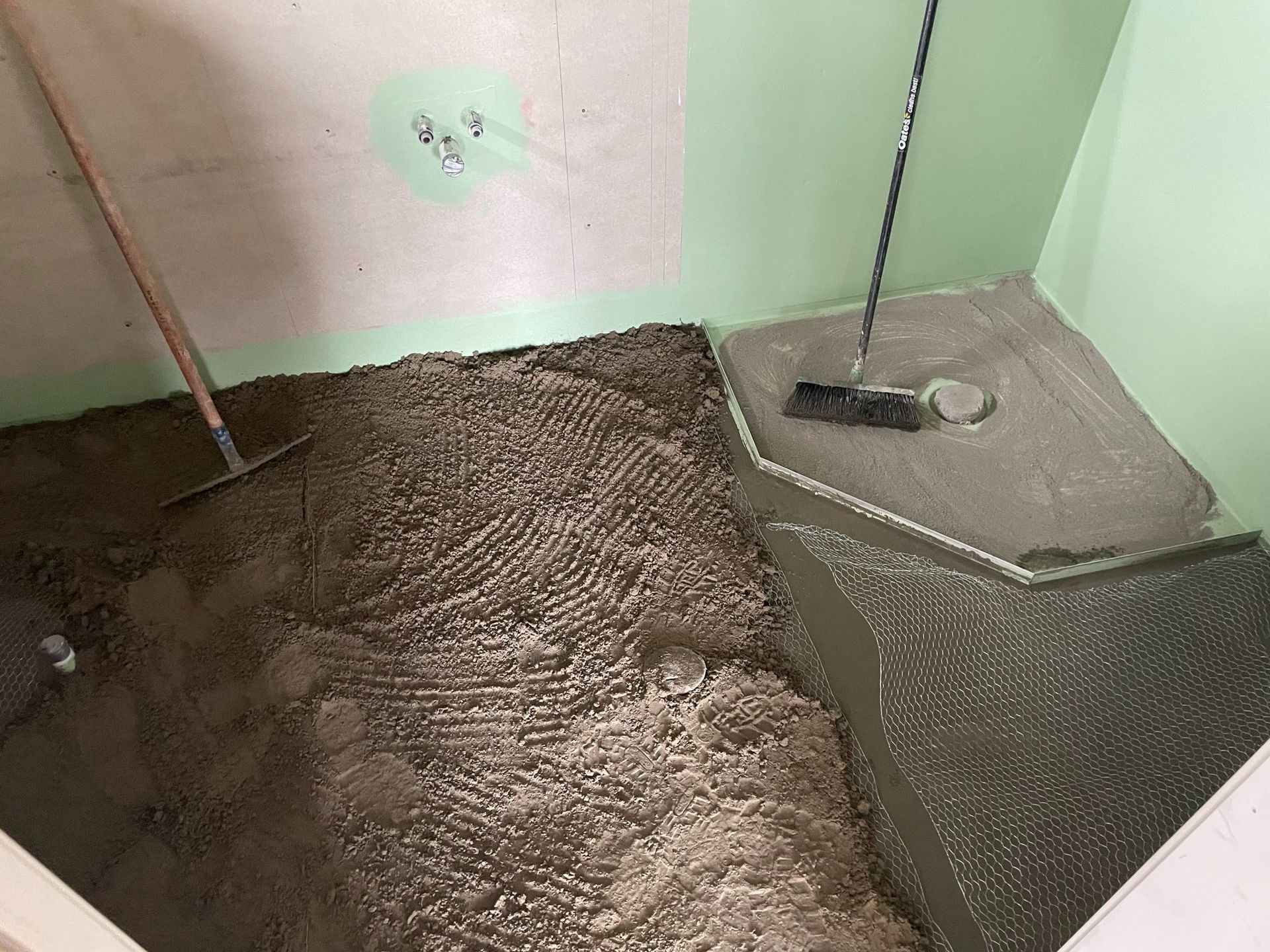 Small corner with a tan rug or bedding beside a gray box and a broom against a pale green wall.