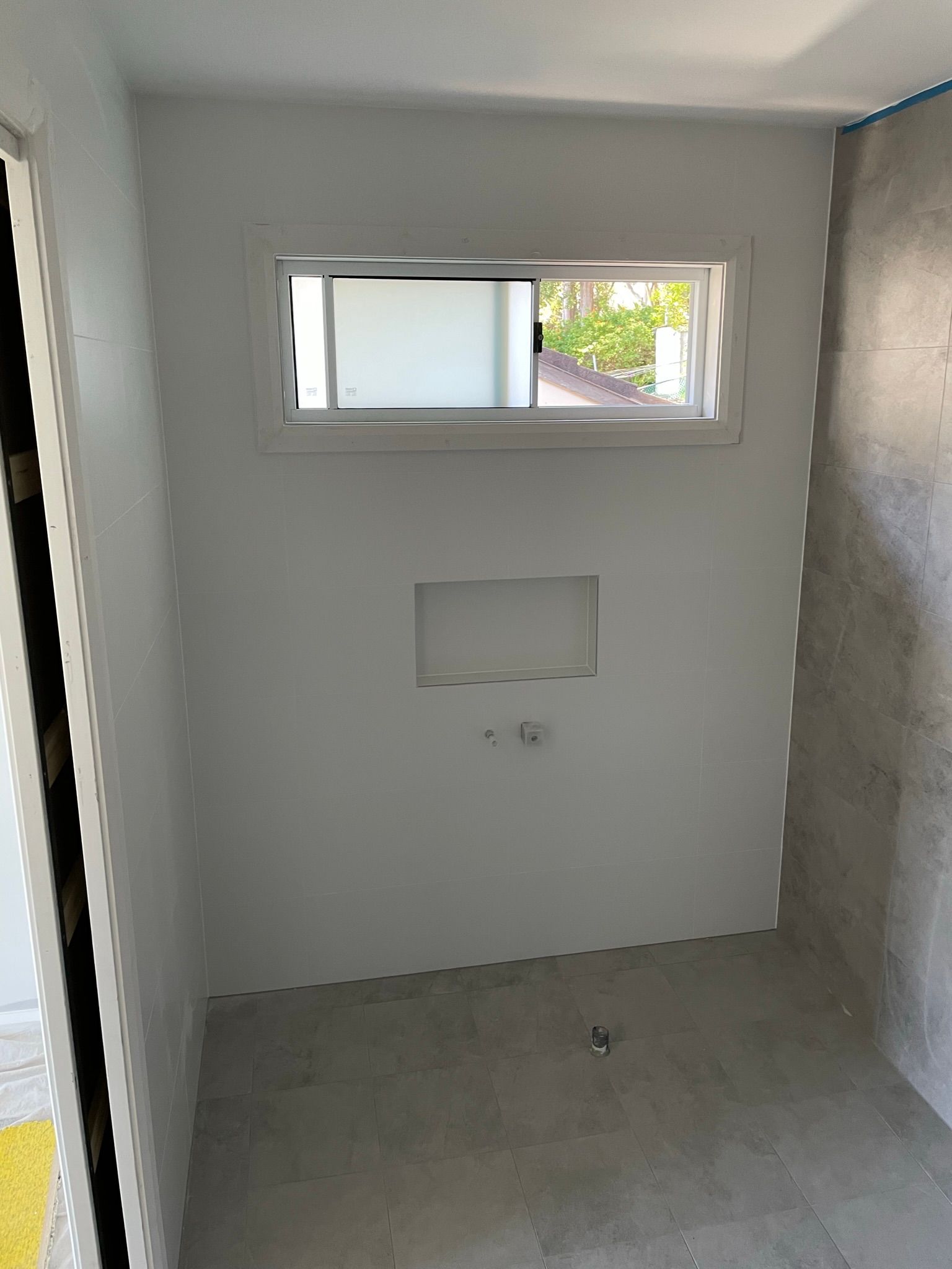 Small unfinished gray room with a narrow high window and wall opening.