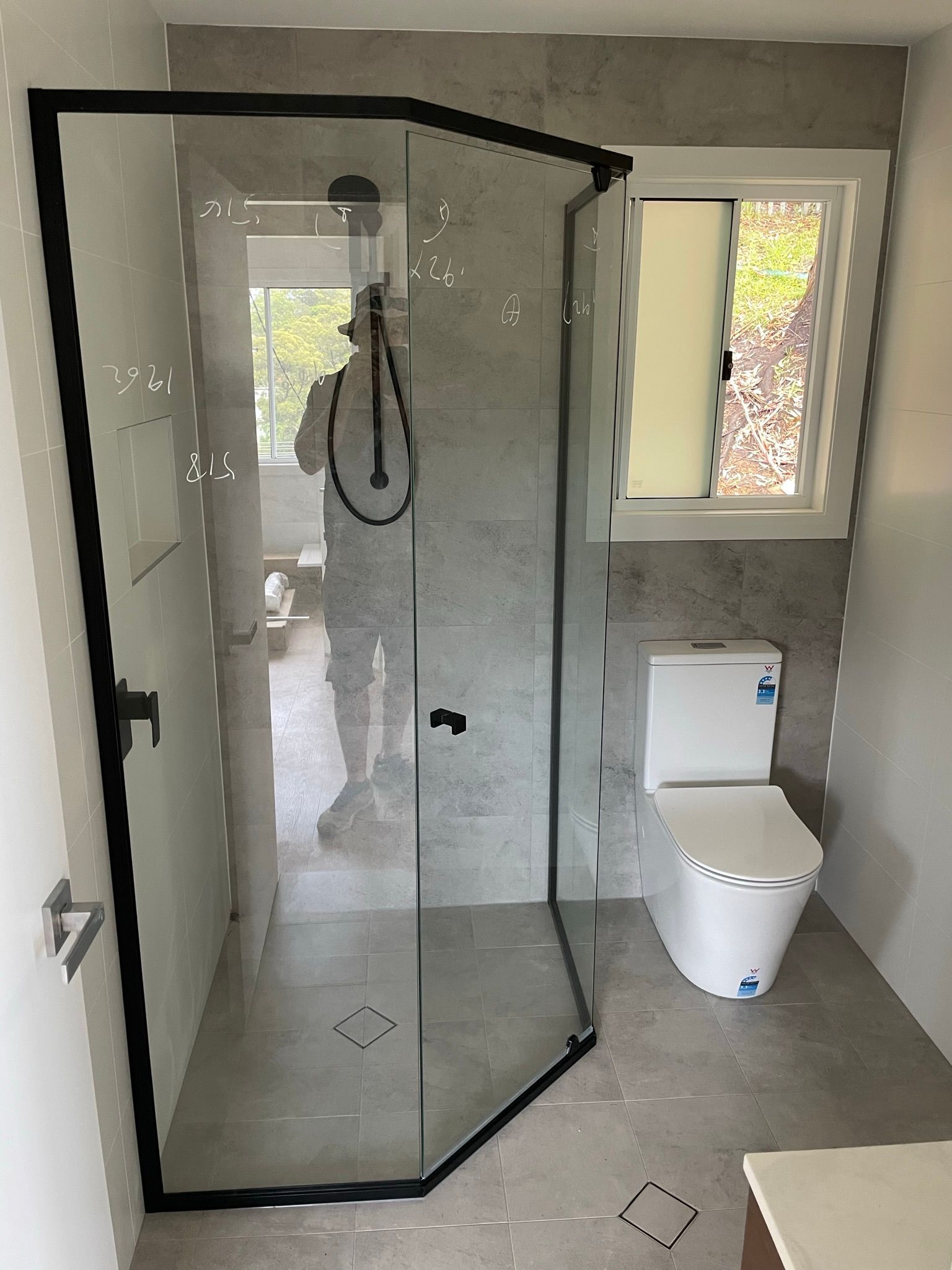 Modern bathroom with glass shower, toilet, and window on tiled walls