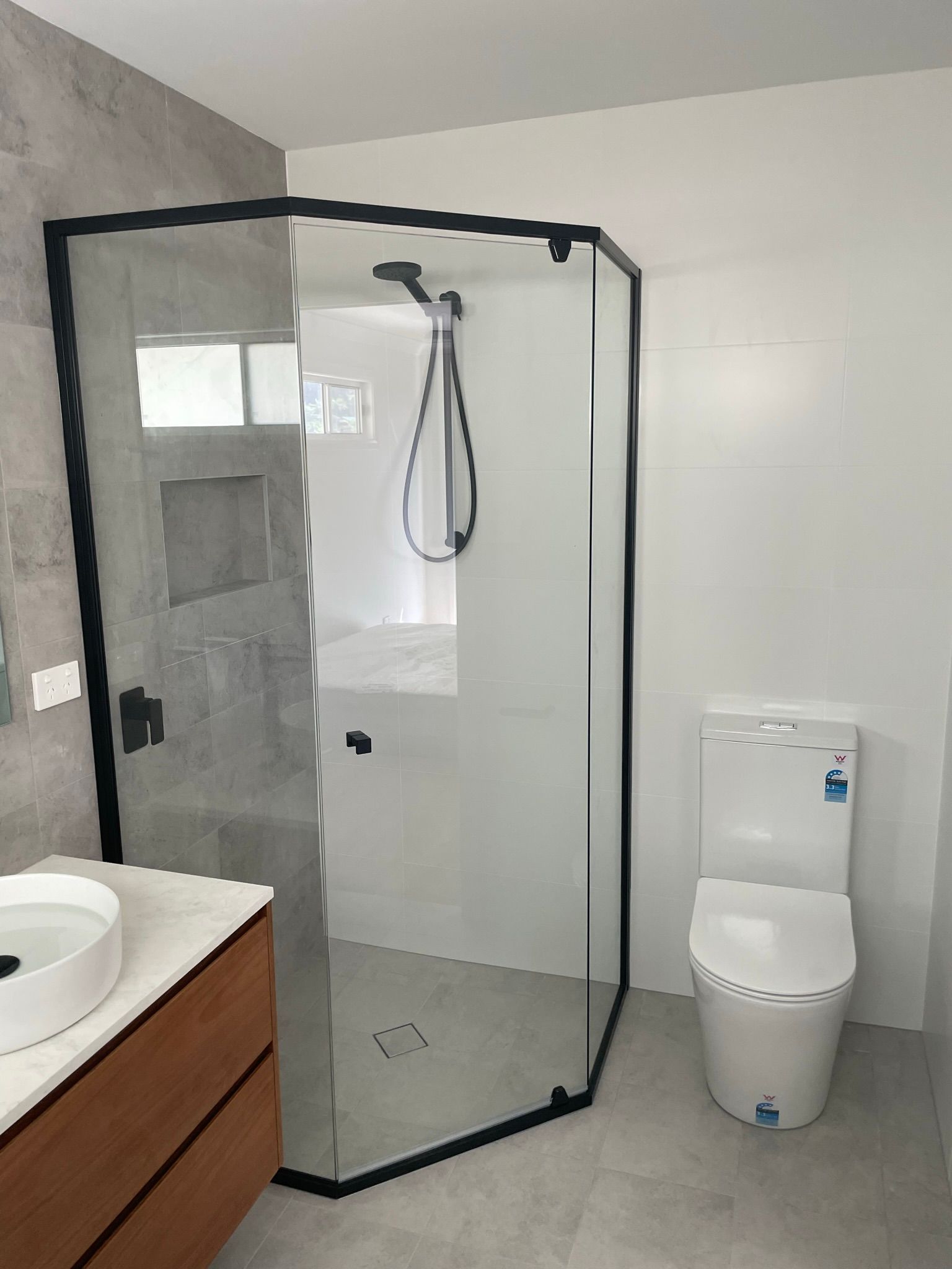 Modern bathroom with a black-framed glass shower, toilet, and vanity sink.