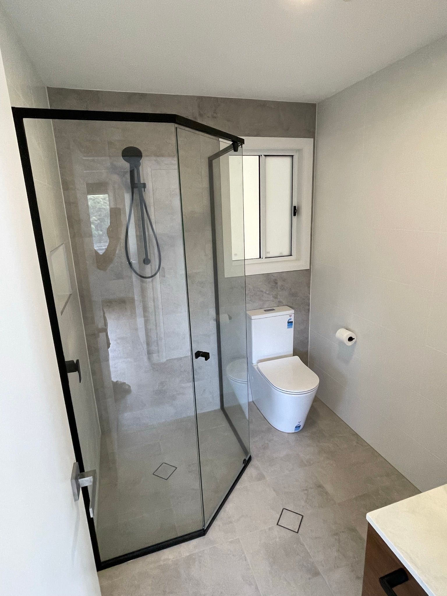 Small bathroom with glass shower enclosure, toilet, sink, and gray walls.