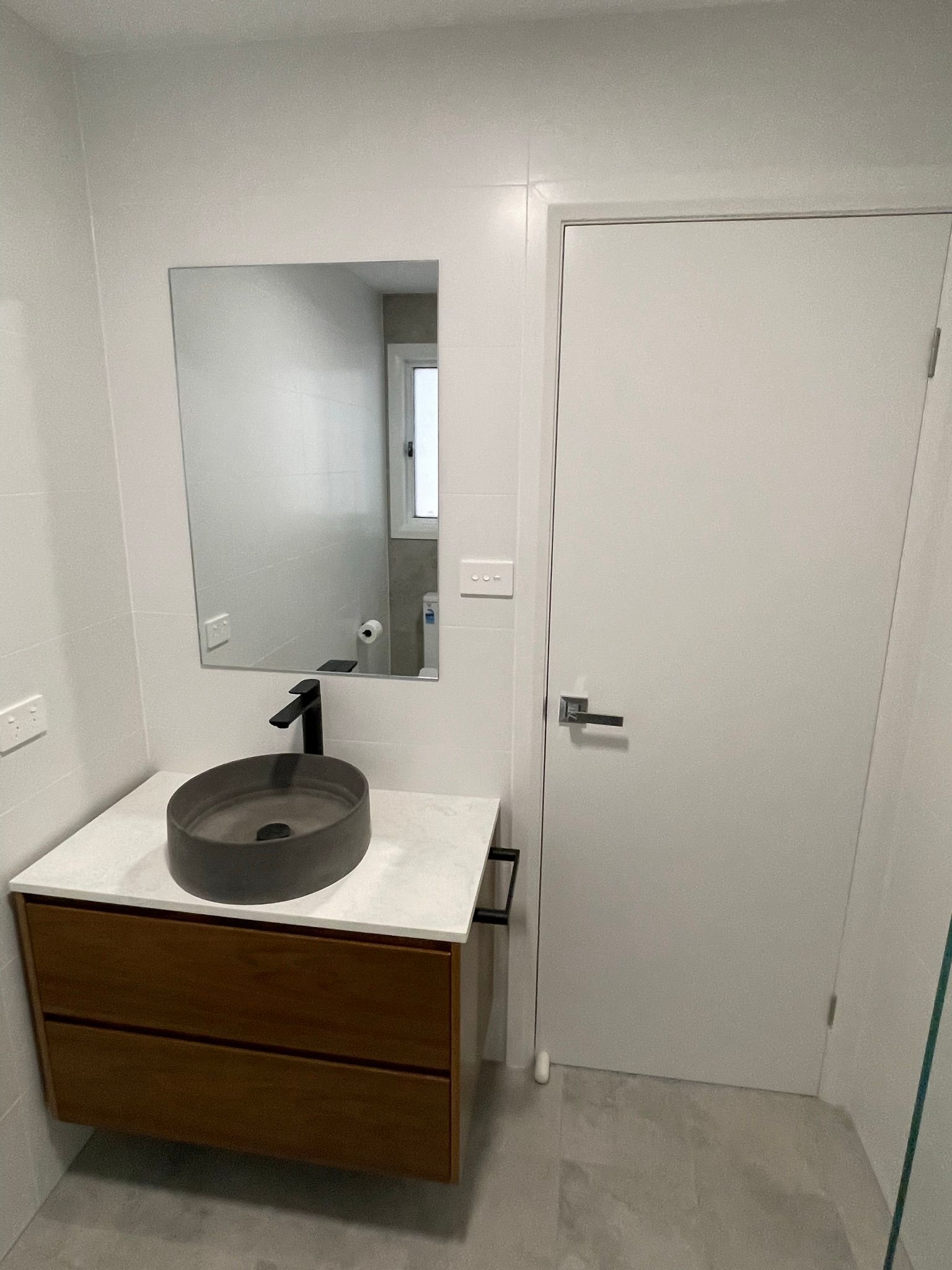 Modern bathroom with floating wood vanity, round black sink, mirror, and closed white door.