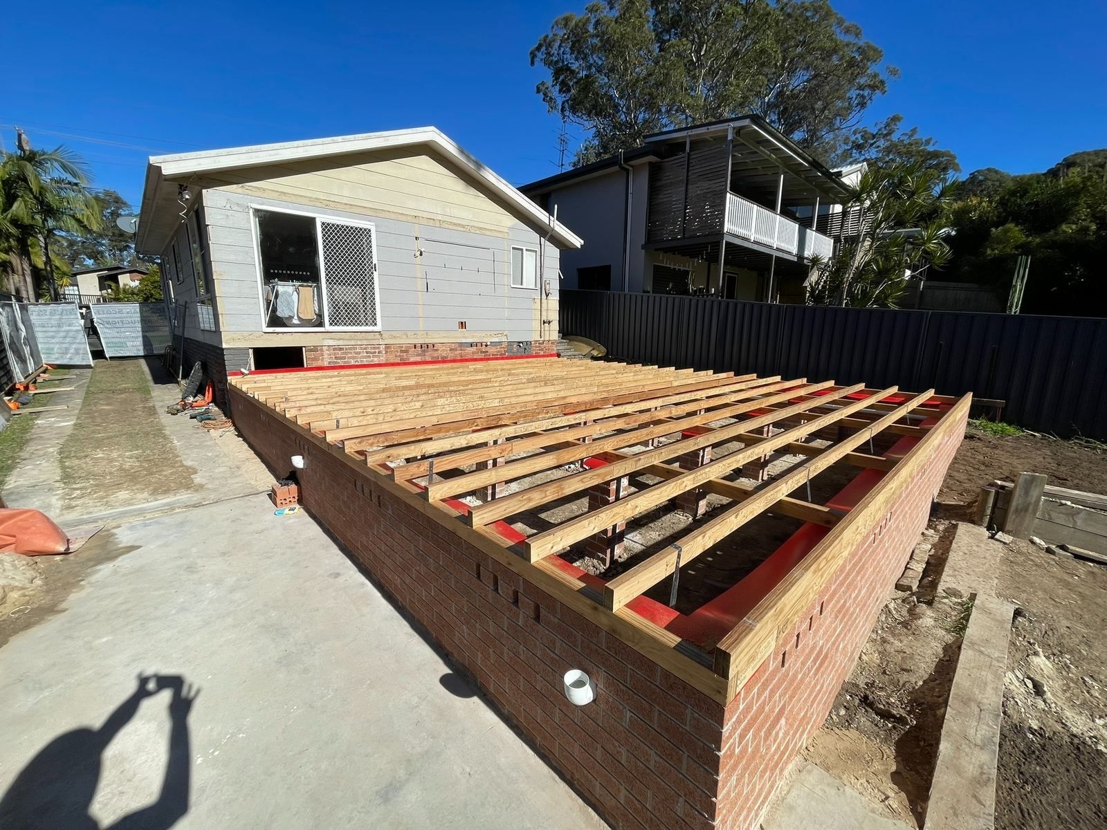 Partially built wooden deck frame beside a brick house in a sunny backyard