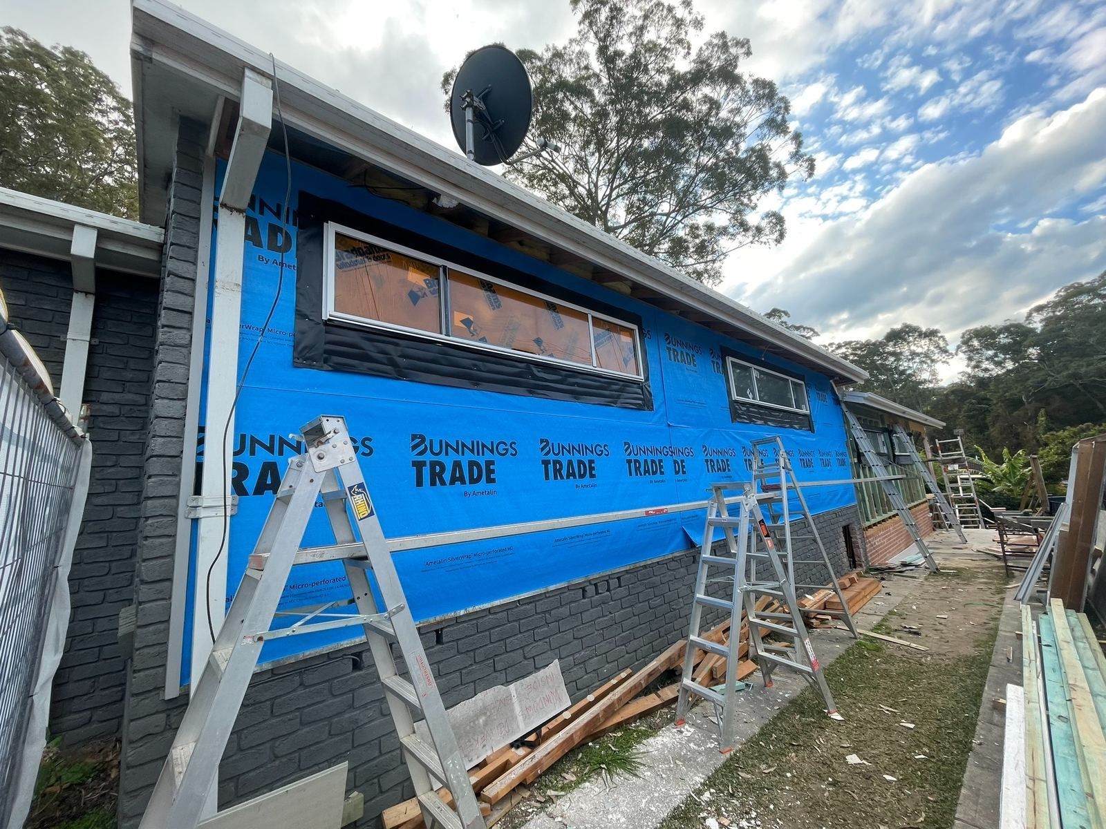 Blue house under construction with ladders and building materials along the side.