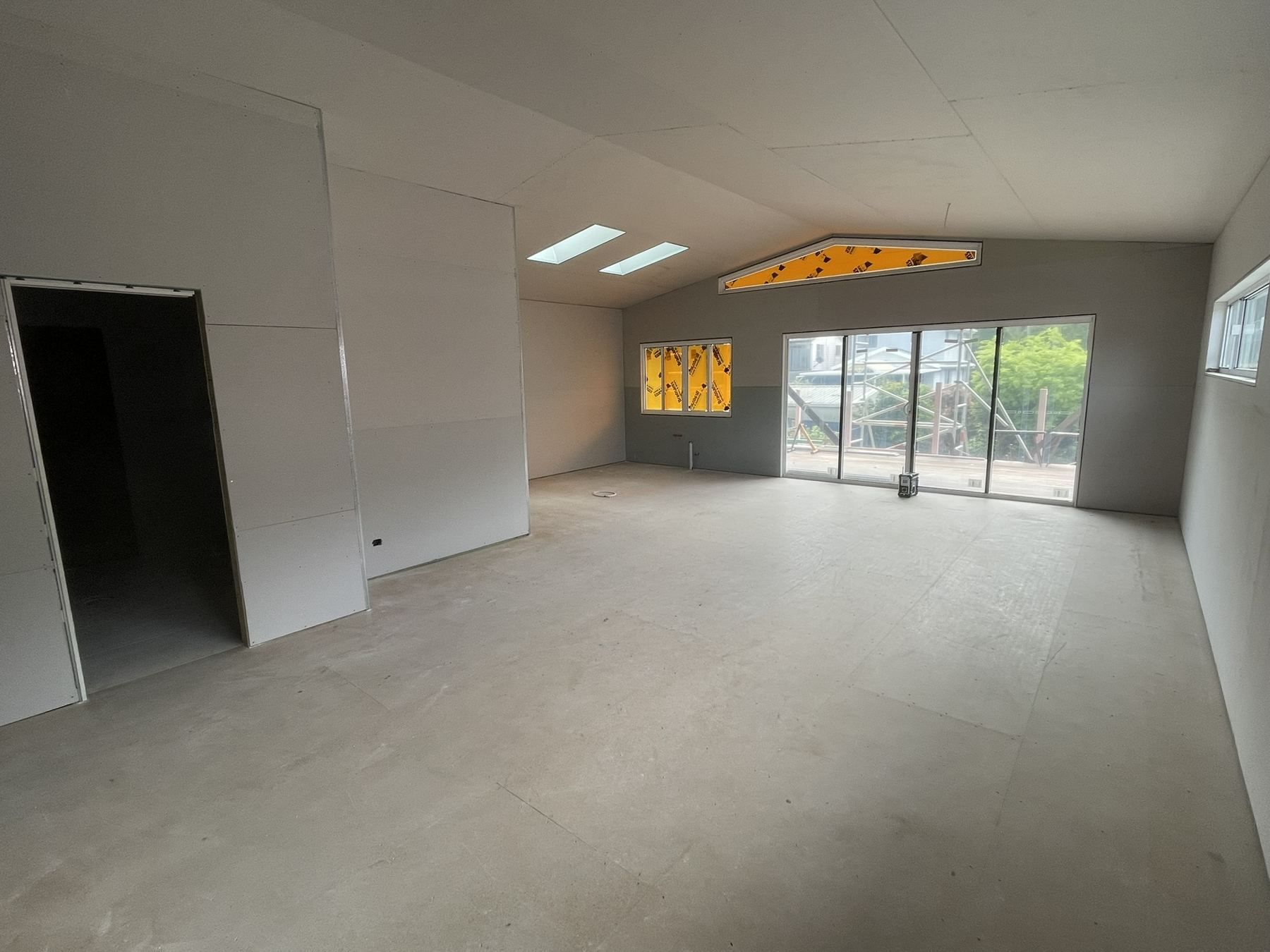 Empty unfurnished room with gray walls, skylights, and large glass doors opening to greenery
