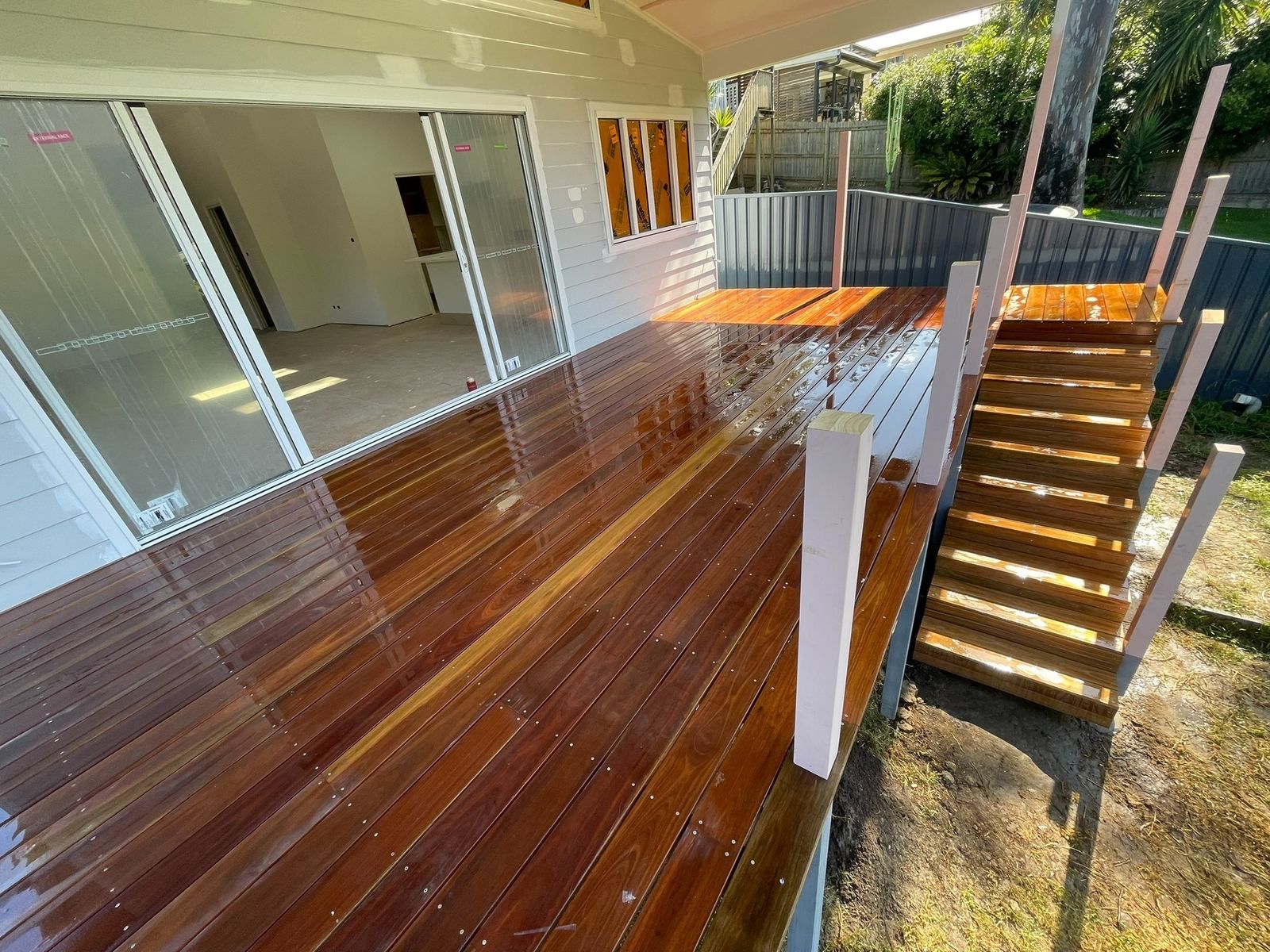 Wooden deck with white railings and stairs beside a house, leading to a fenced yard.