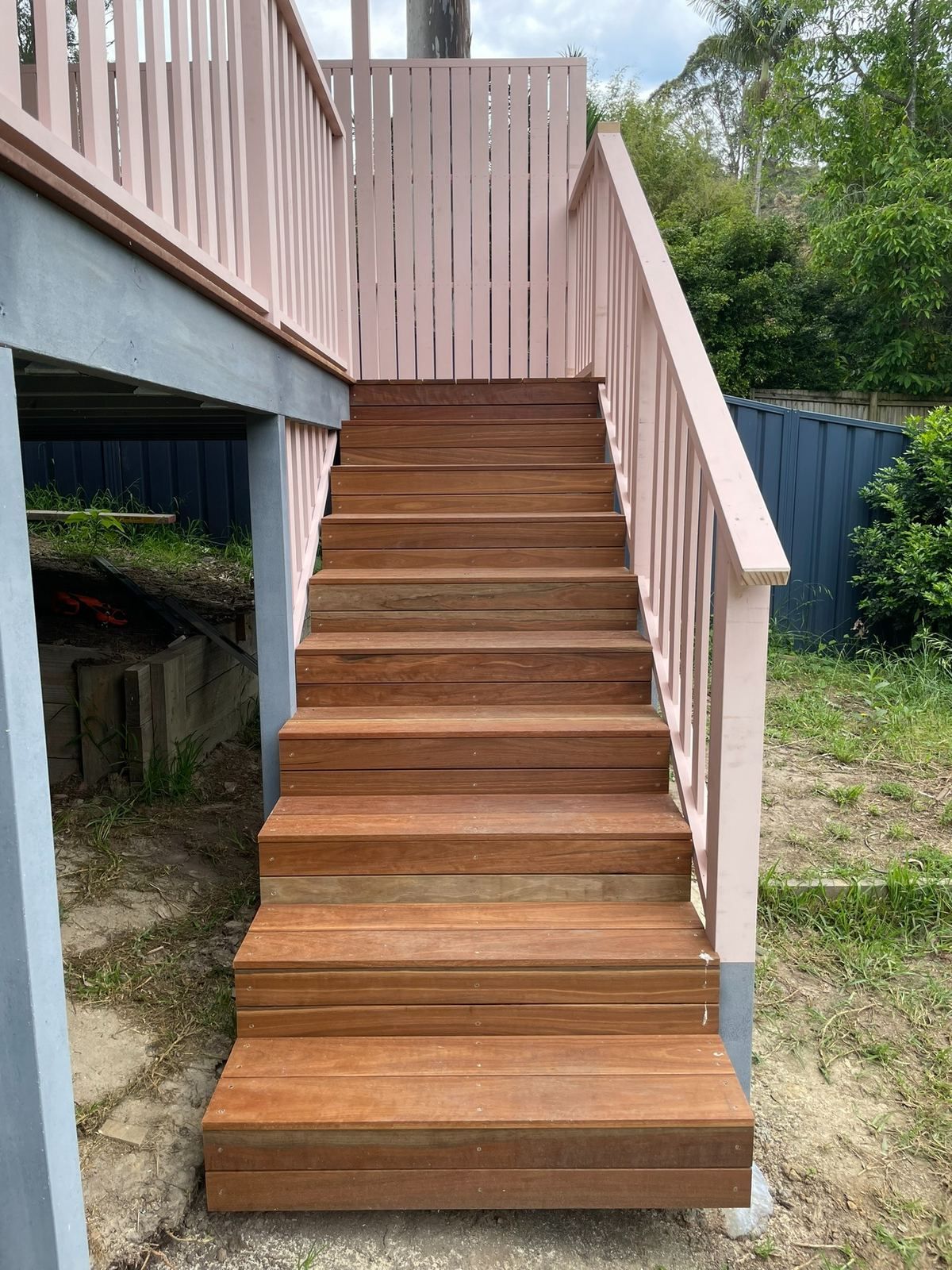 Wooden outdoor staircase with pink railings leading up to a raised deck in a backyard.