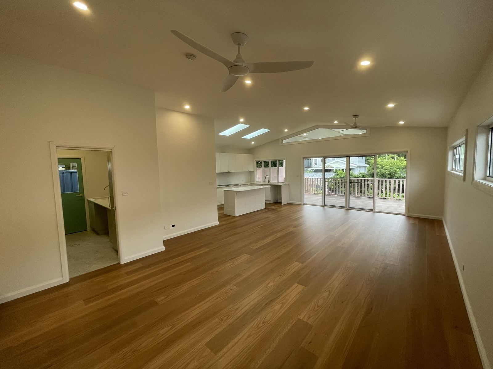 Empty living room with wood floors, white walls, ceiling fan, and sliding doors to a deck.