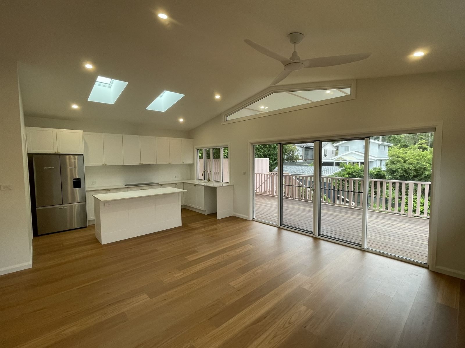Empty modern open-plan kitchen and living area with wood floors, white cabinets, and sliding doors to a balcony