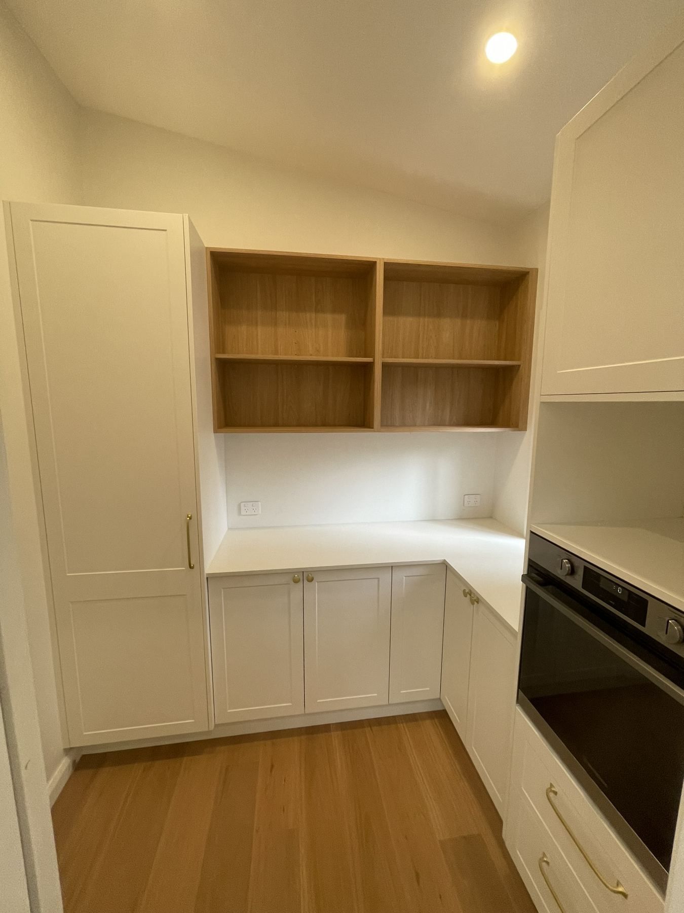 Small modern kitchen with white cabinets, open wood shelves, and a built-in oven