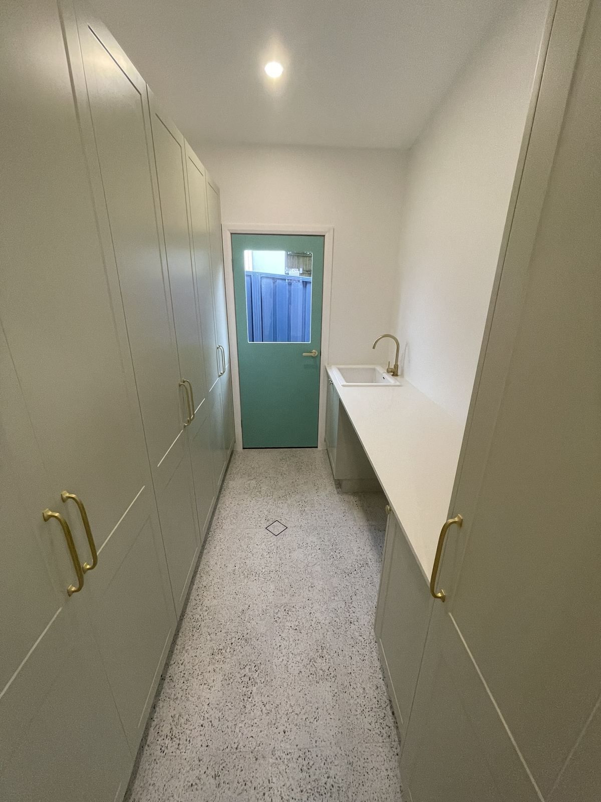 Narrow hallway with built-in cabinets, white countertop, and a teal door with a blue curtain at the end.